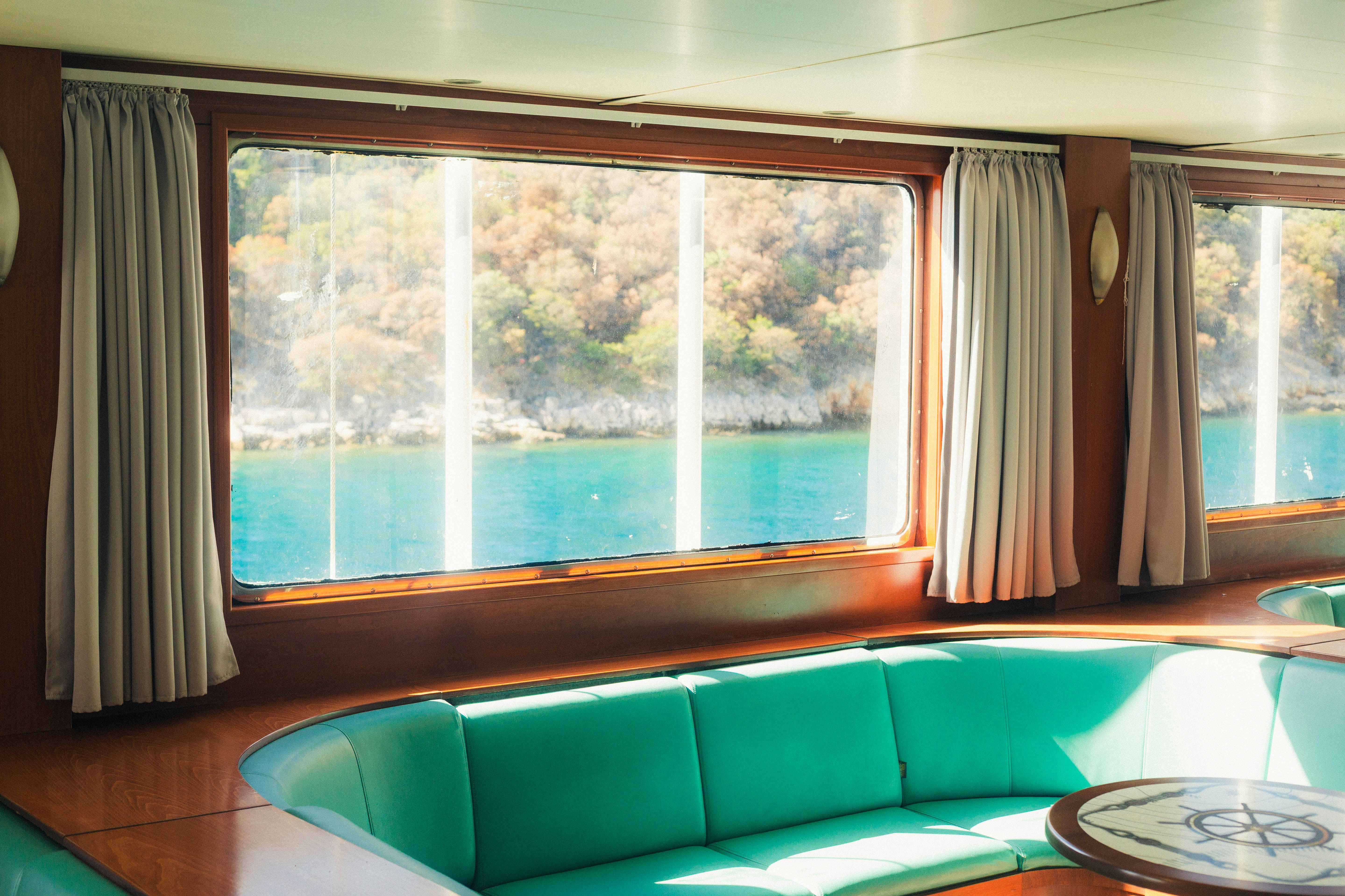 A turquoise curved sofa in a wood-paneled cabin overlooking a sunny coastal landscape