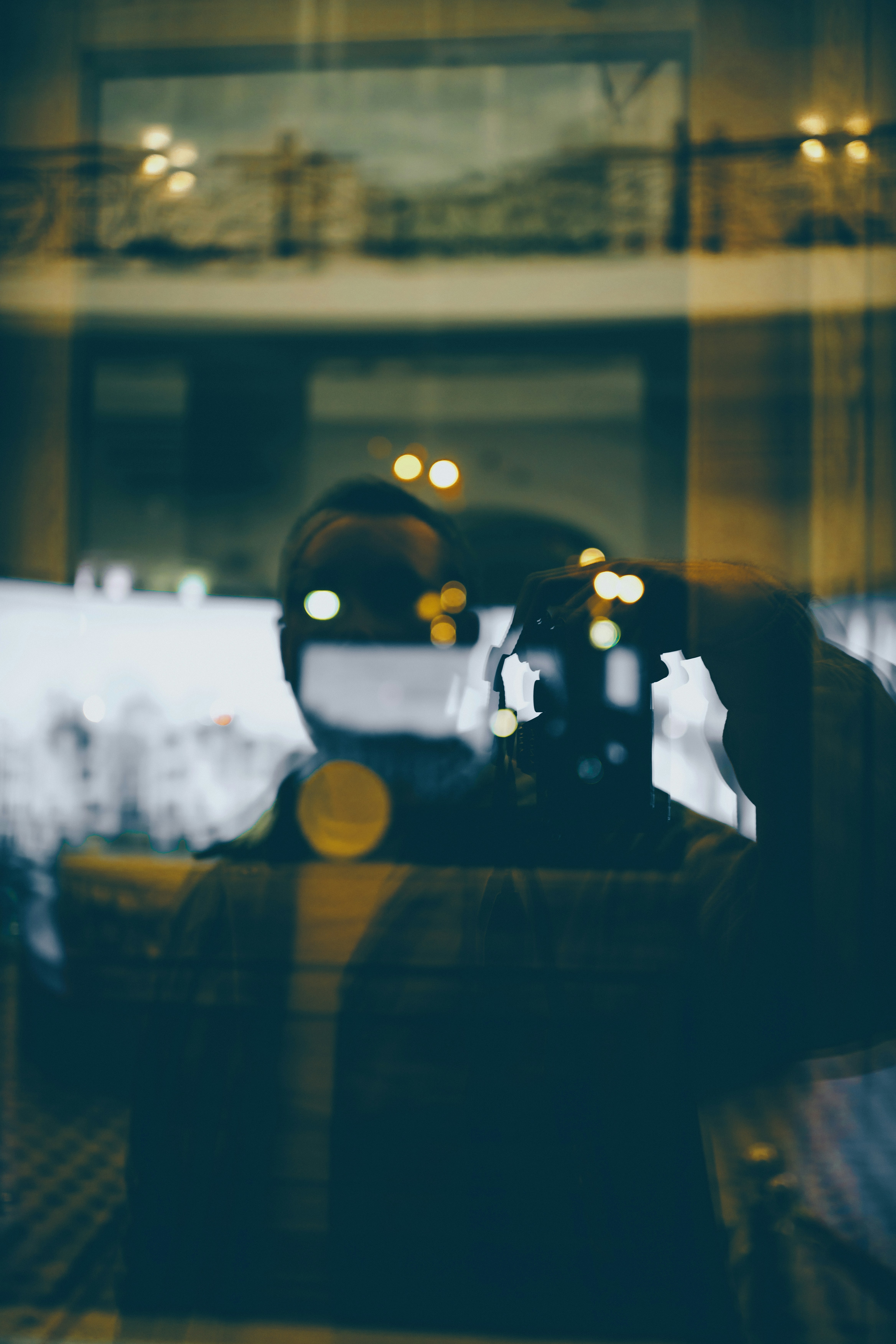 A person holding a camera reflected in a glass window with bokeh lights