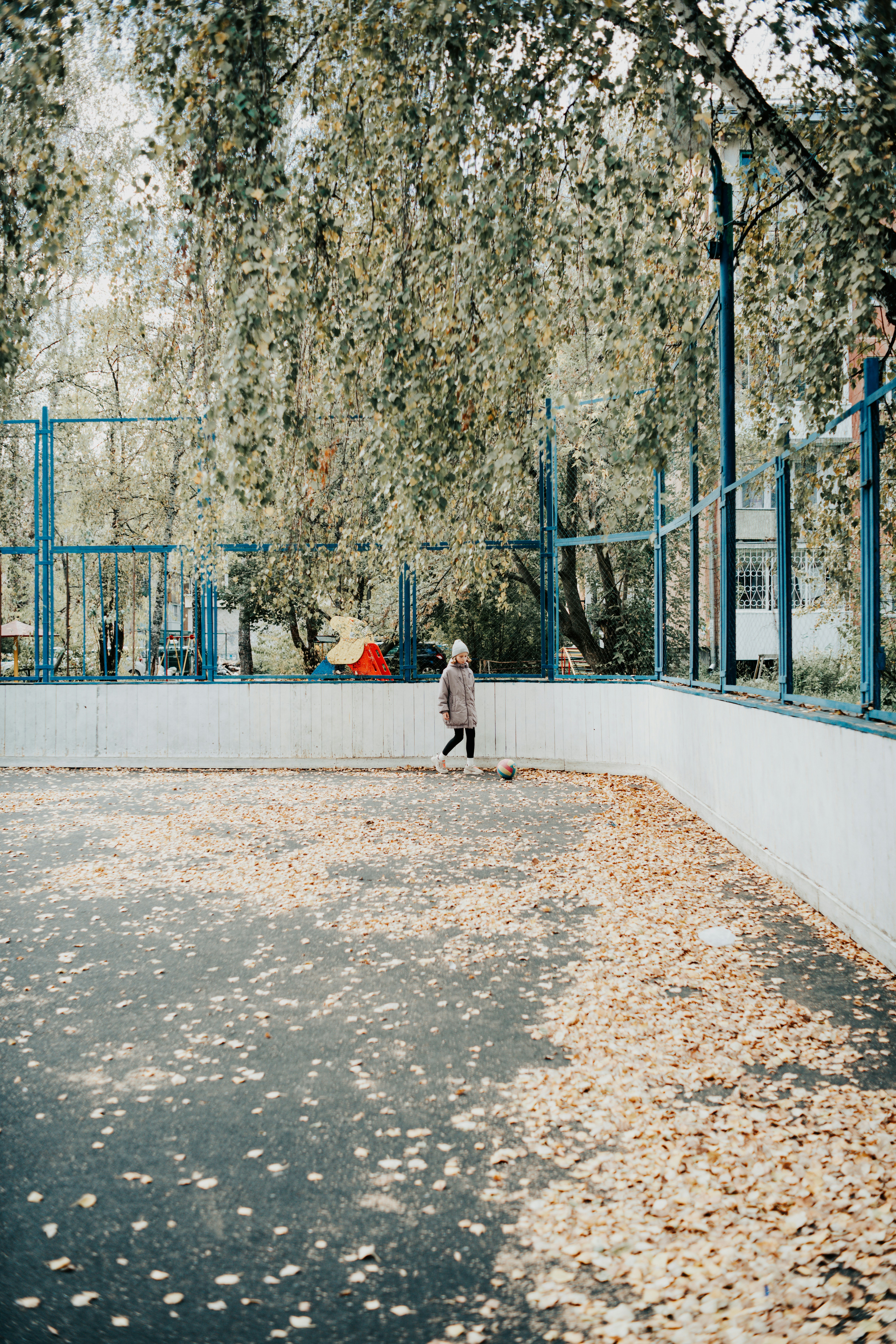 A child in a winter coat playing with a ball on an autumn court