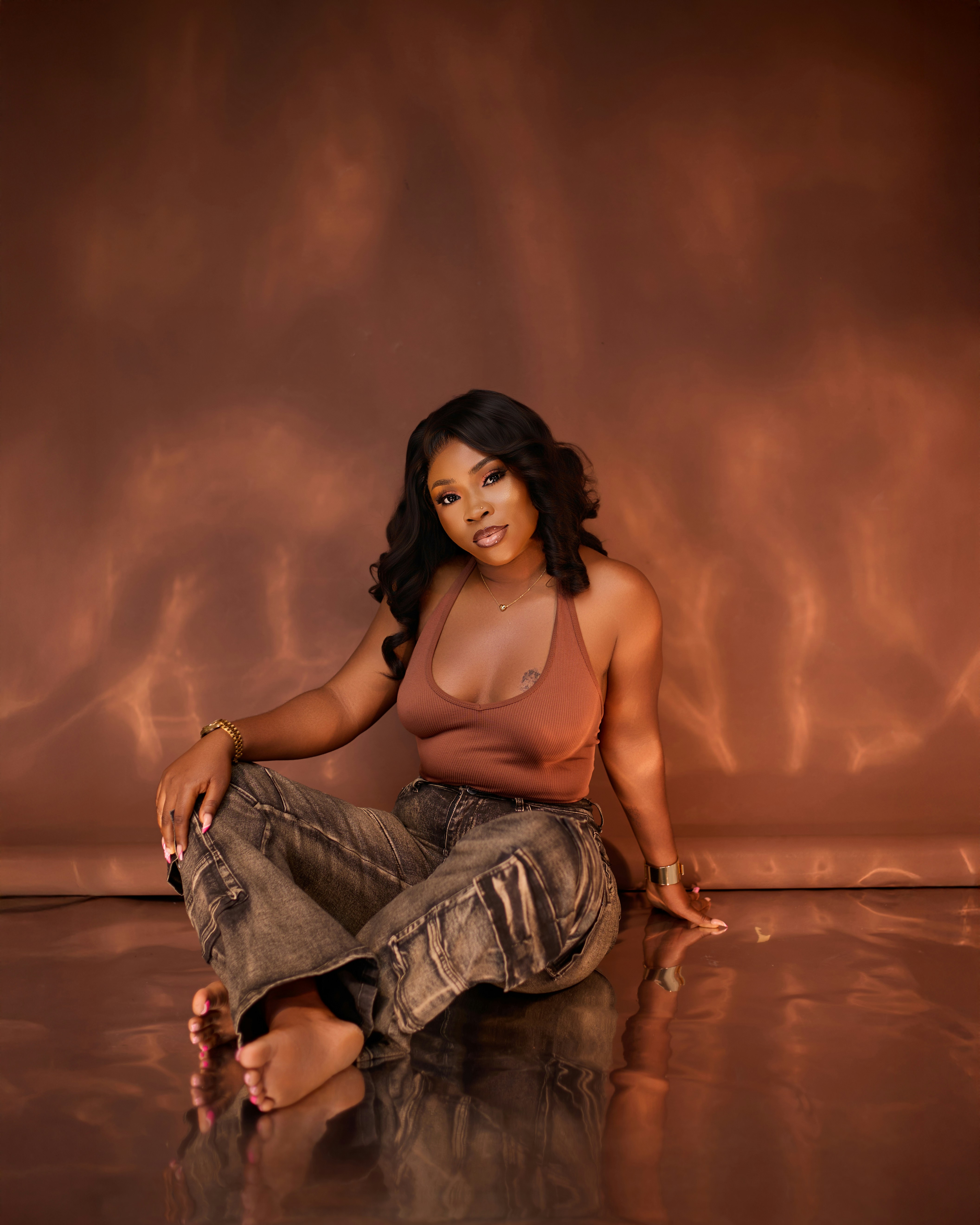 A woman in a brown halter top and jeans sitting on a reflective surface