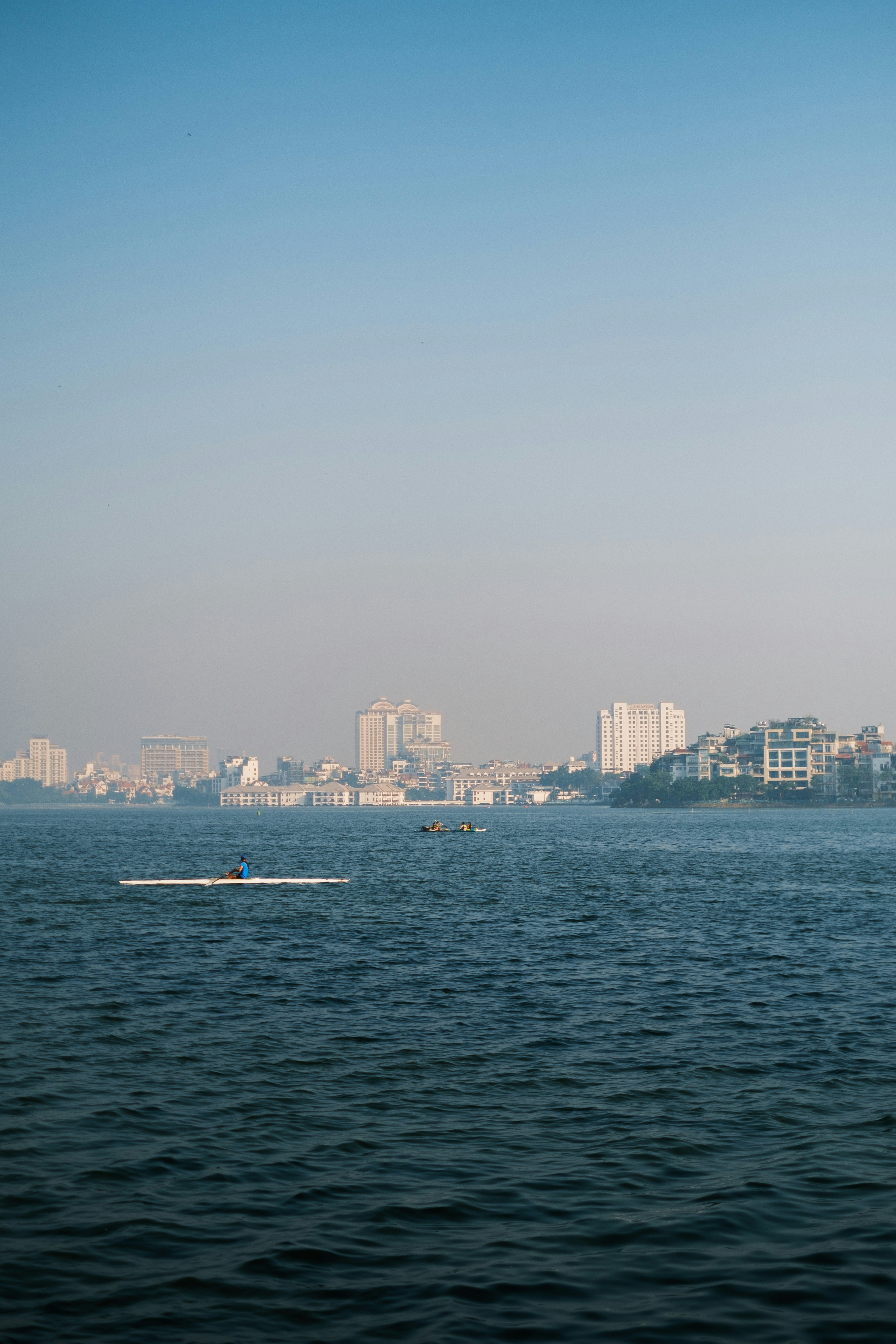 A person rowing a scull on a large lake with a distant city skyline