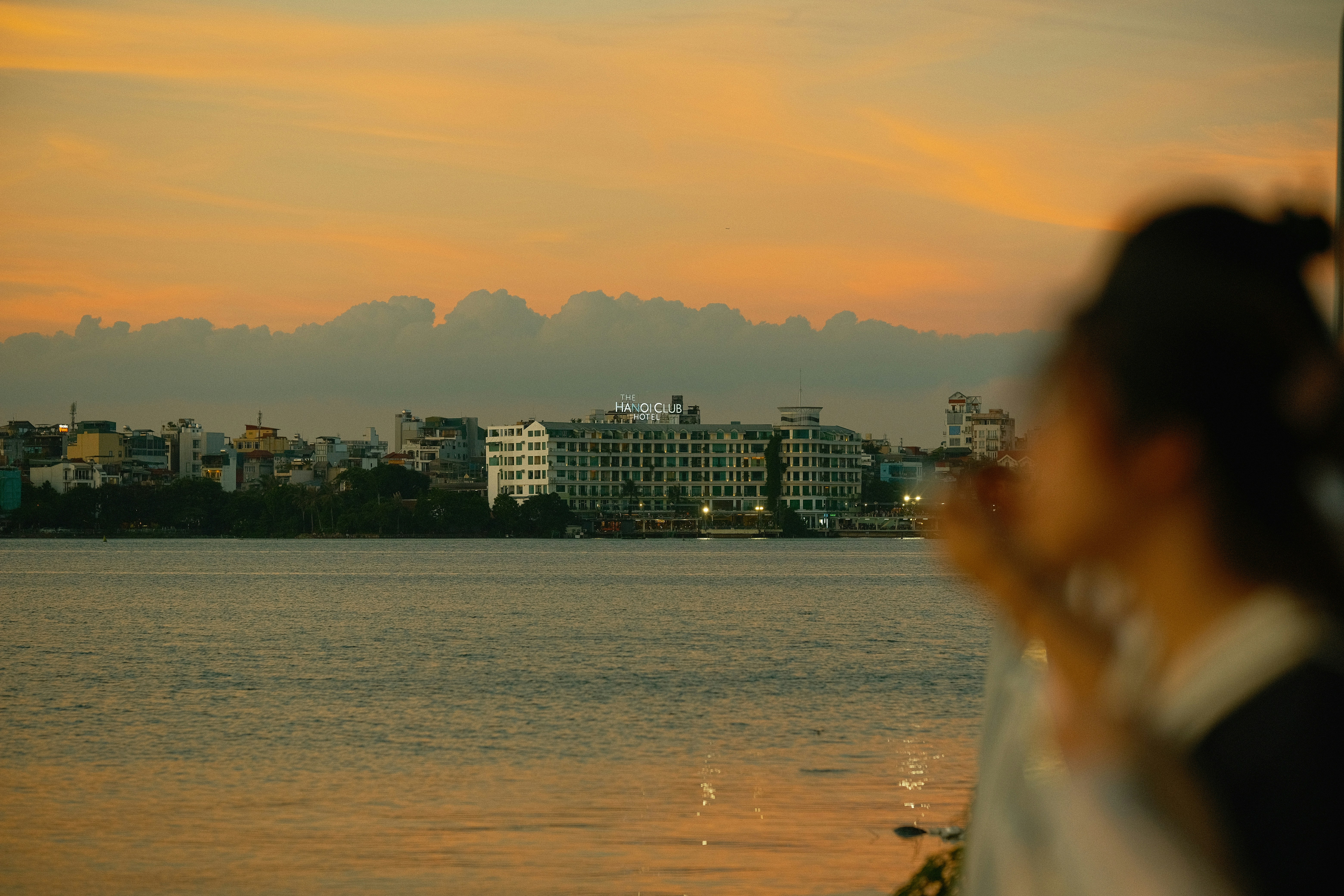 The Hanoi Club Hotel across a lake under a warm orange sky