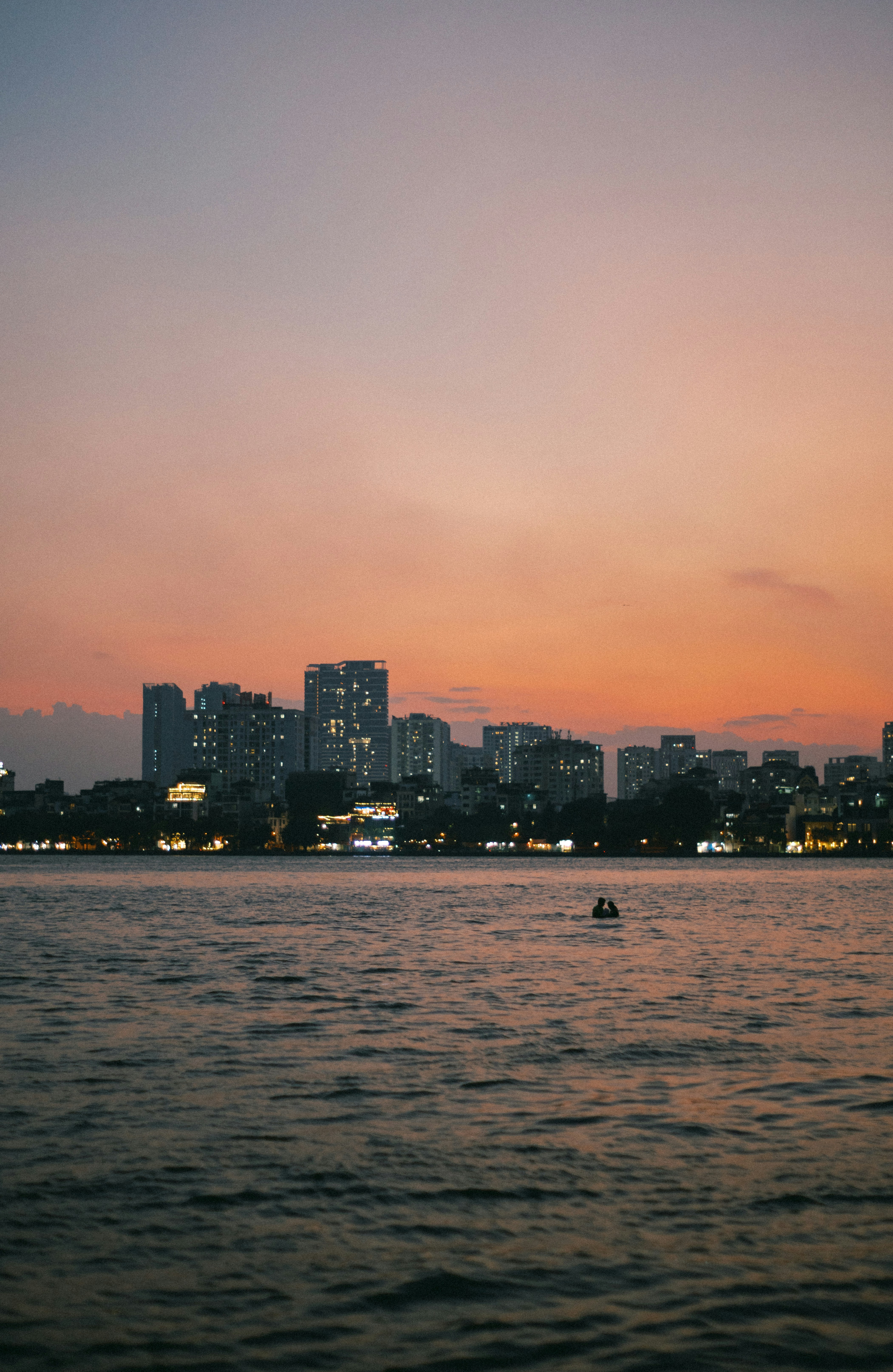 A person swimming in a lake before a city skyline at golden hour