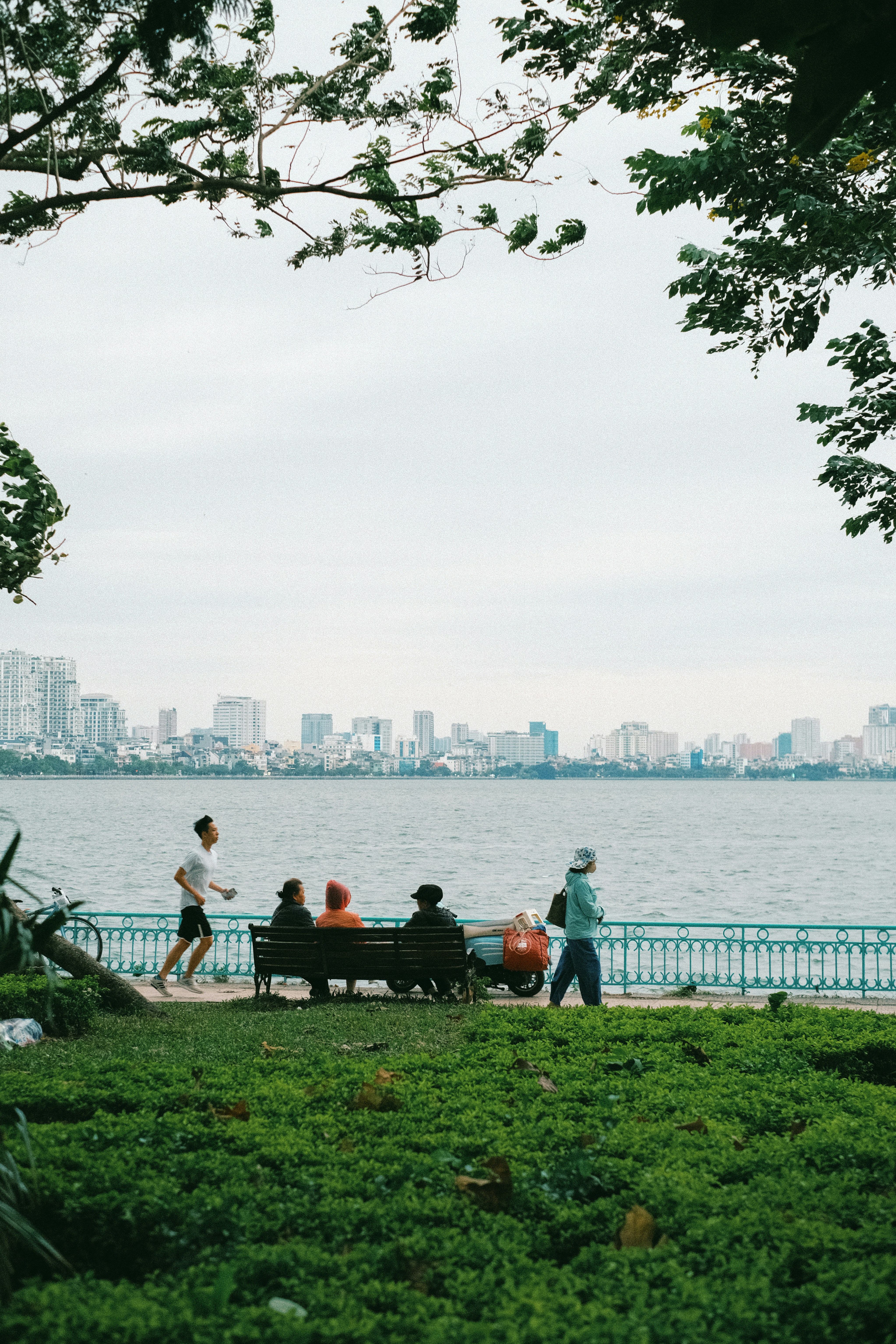 A person jogging past people on a bench by a large lake in Hanoi