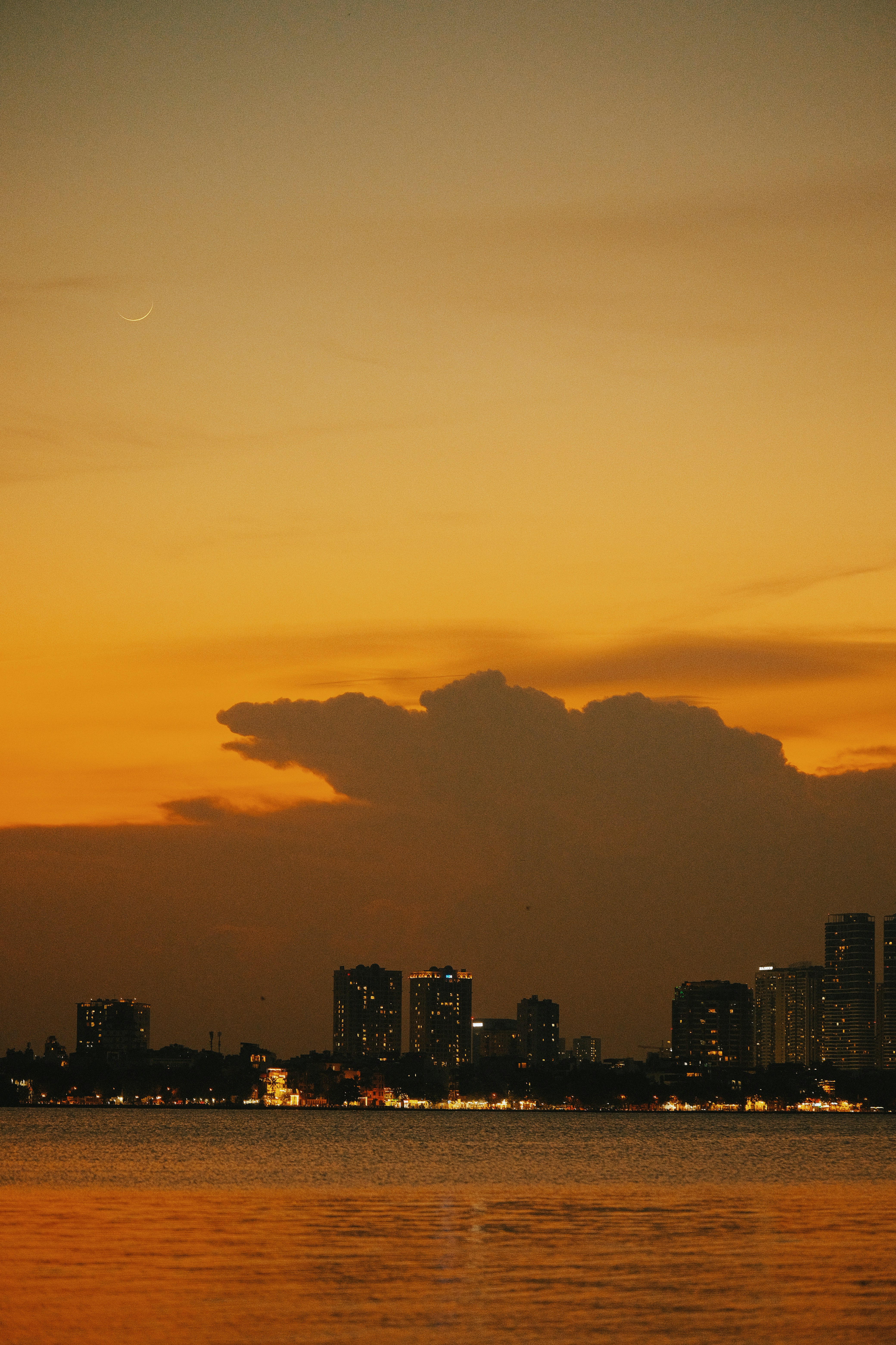 A crescent moon above a city skyline silhouetted against a warm orange sky