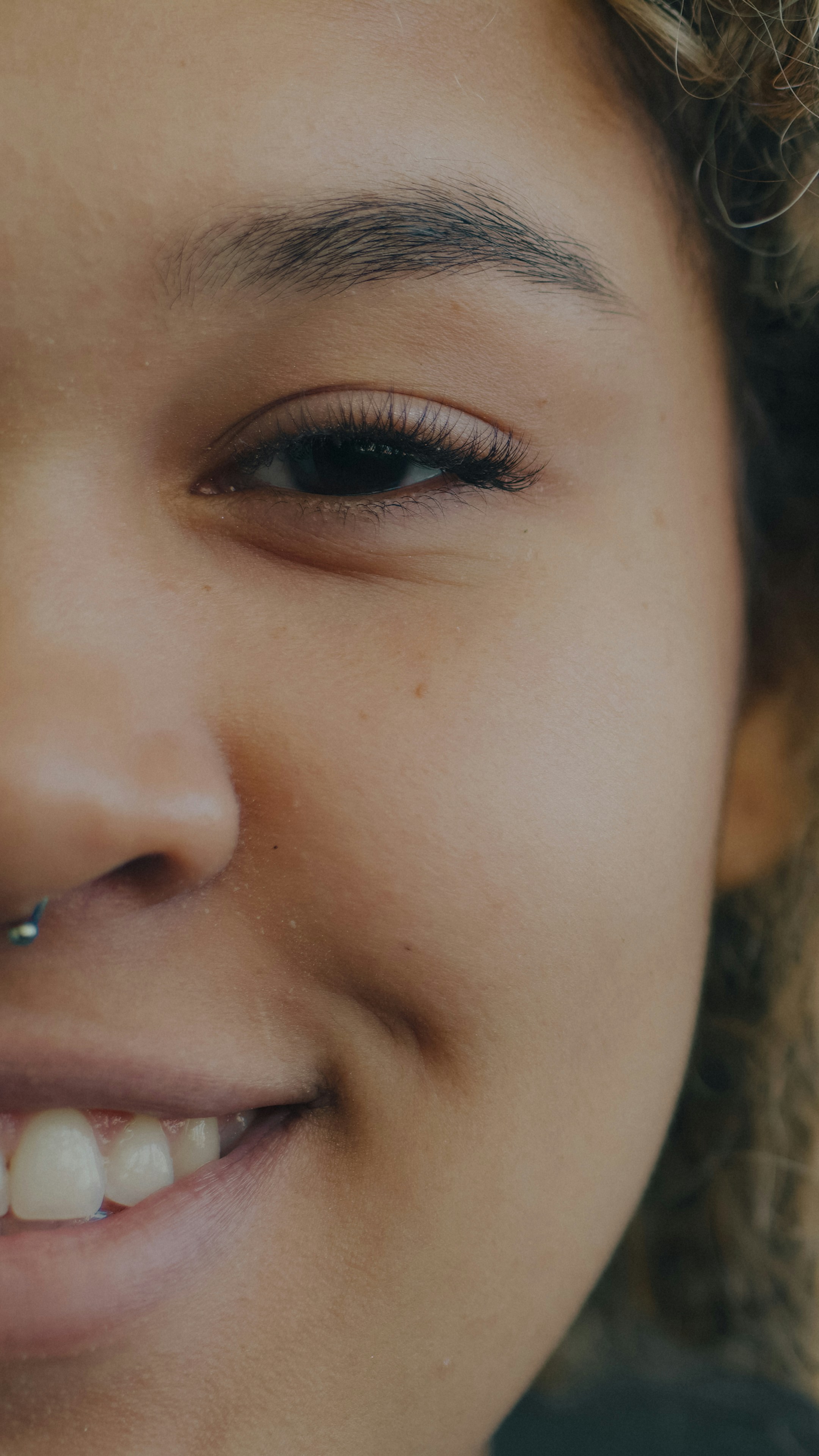 A close-up of a smiling person with a silver septum piercing
