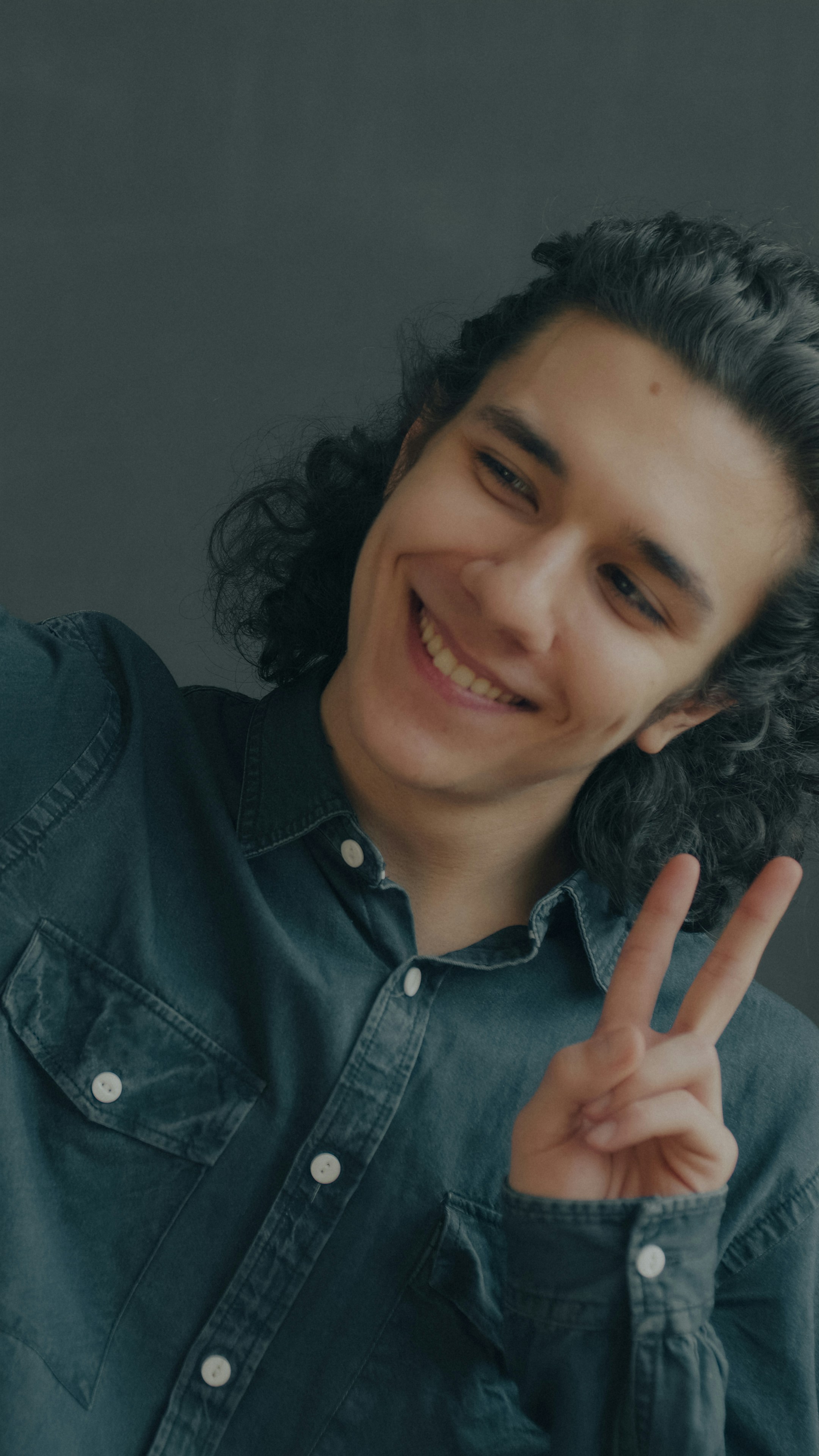 Una persona sorridente con lunghi capelli scuri che fa il segno della pace
