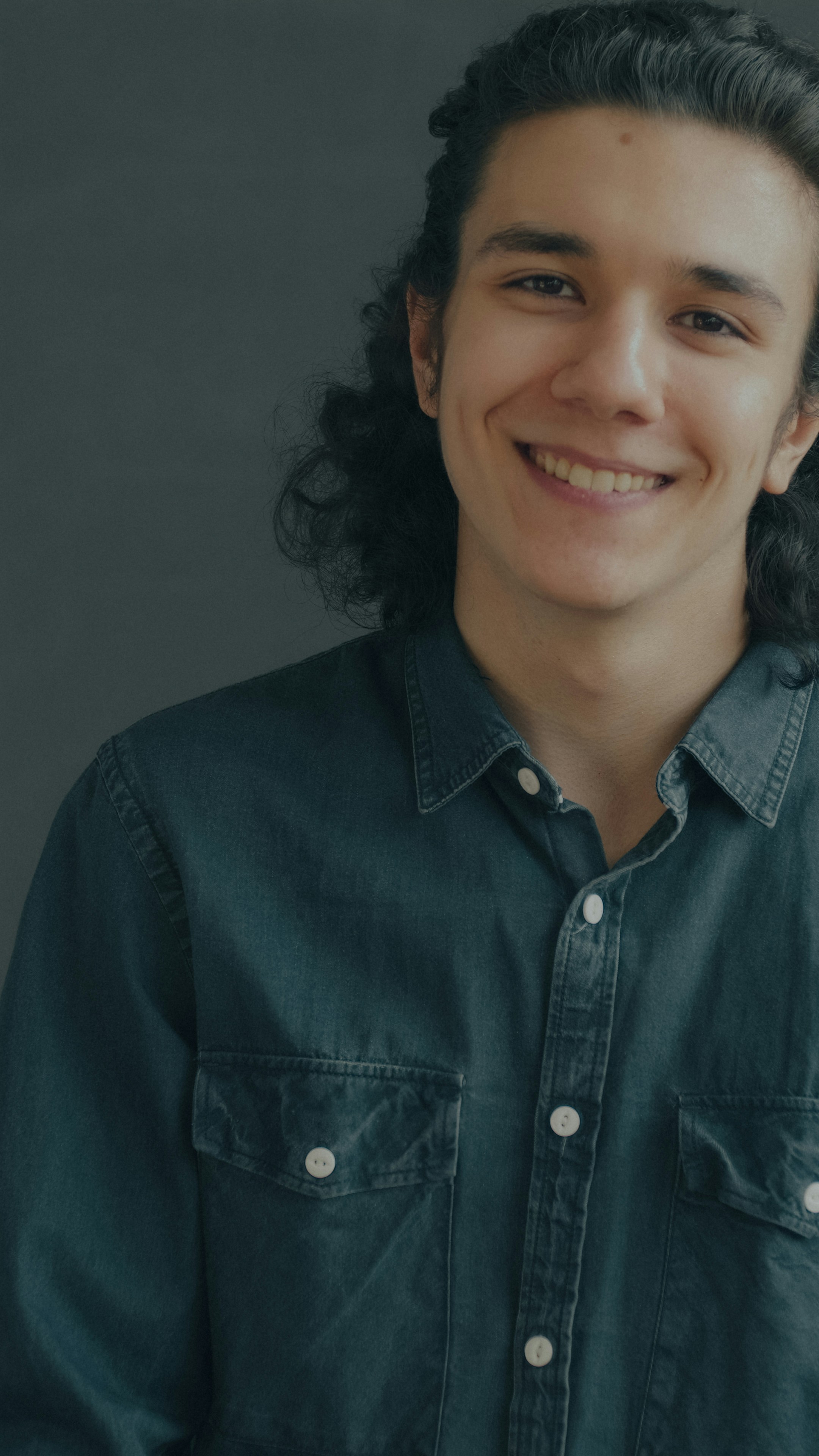 Una persona sorridente con lunghi capelli scuri che indossava una camicia scura abbottonata