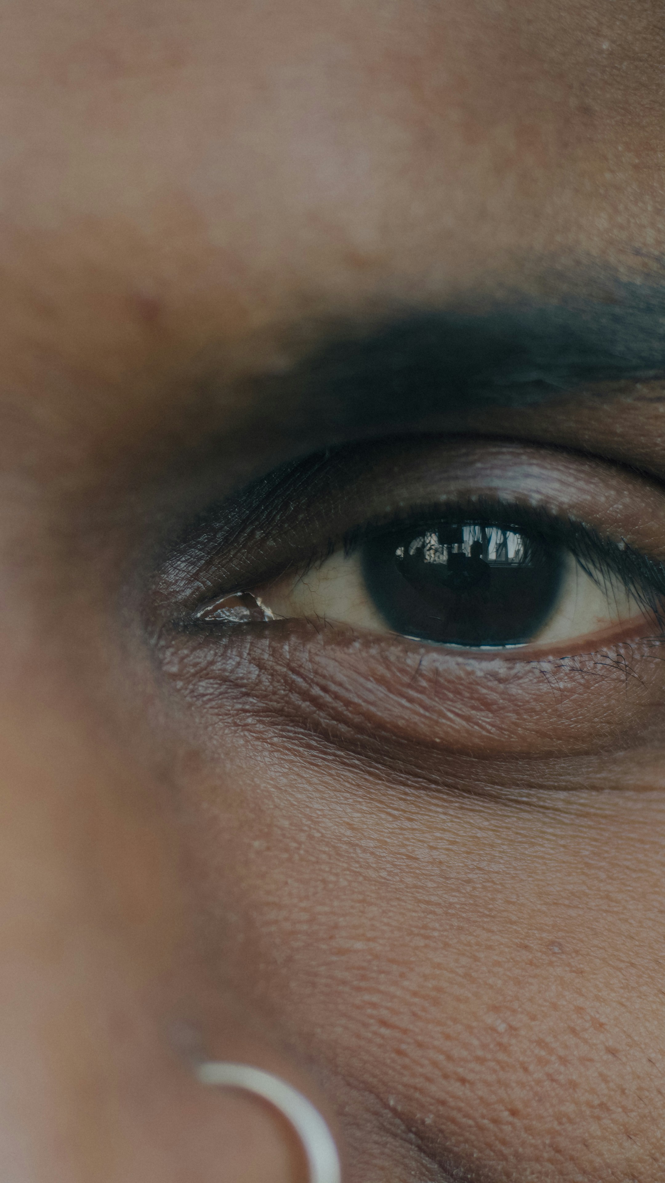 A close-up of a dark brown eye with a small silver hoop earring