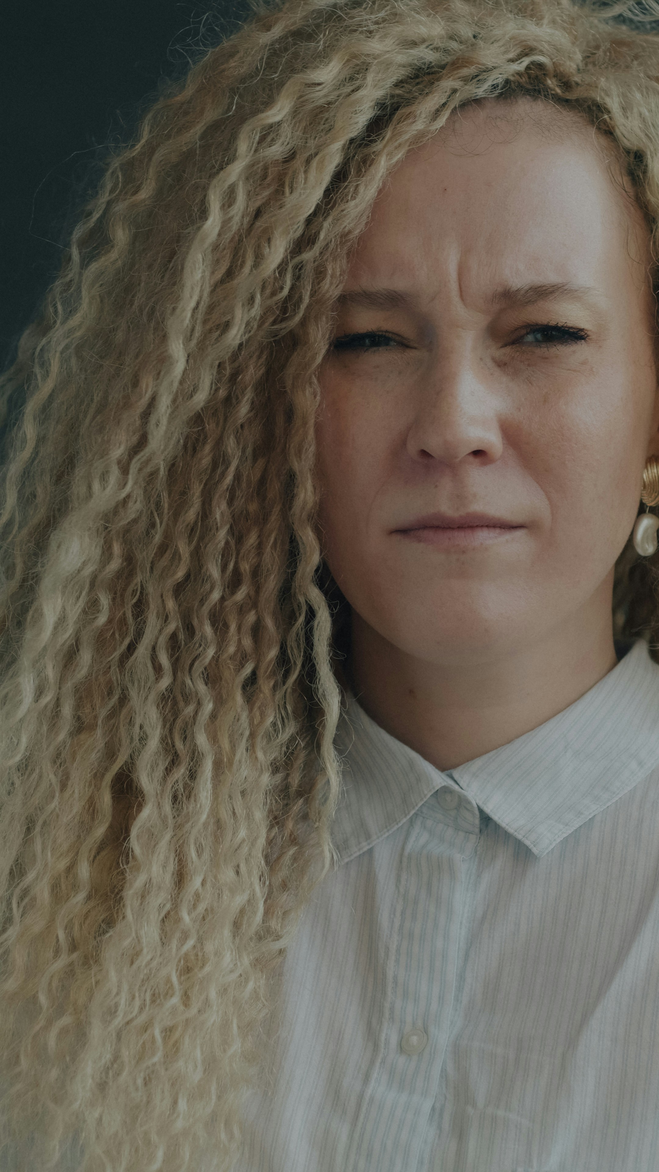 A woman with long blonde curly hair wearing a light blue collared shirt