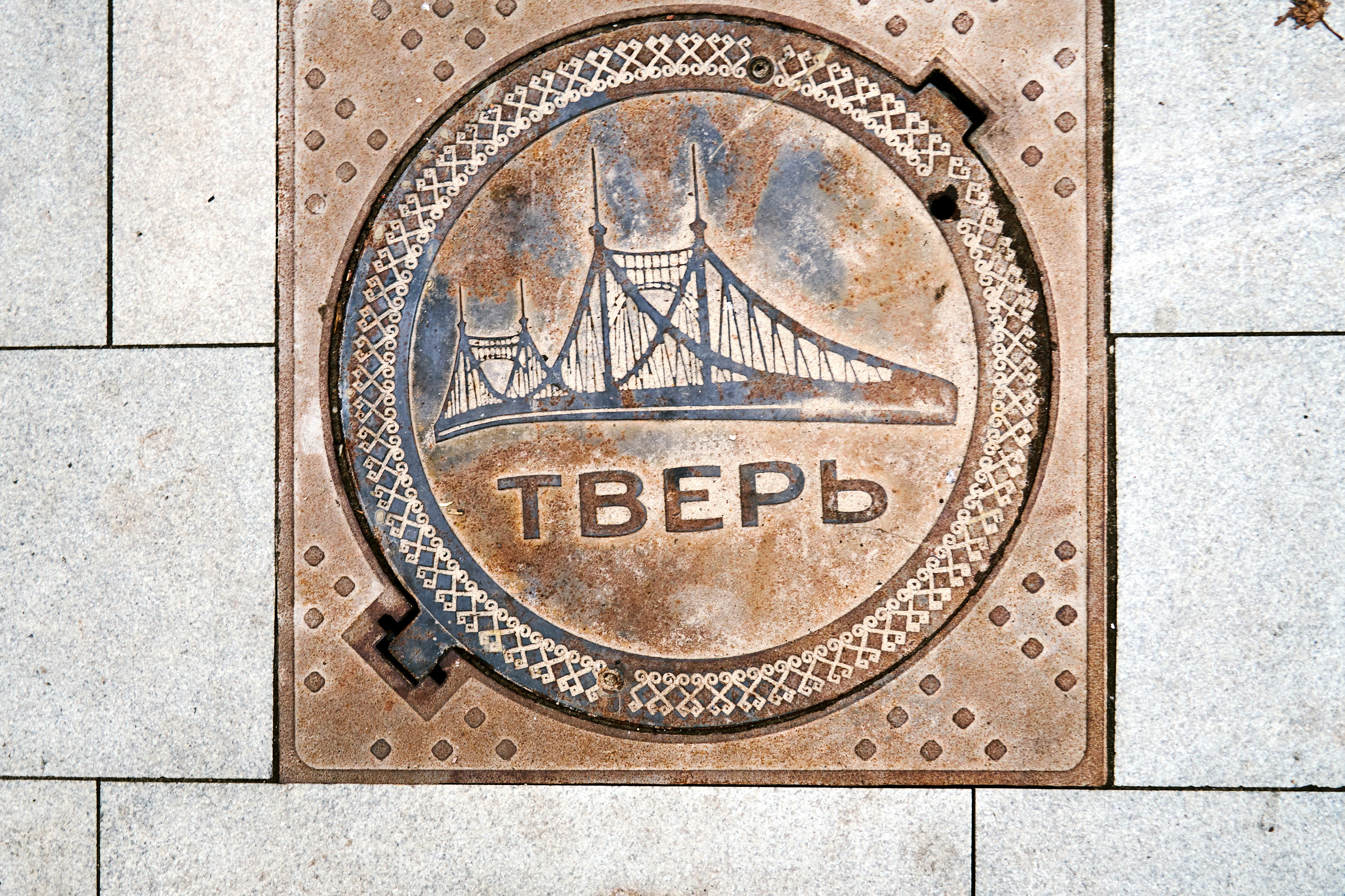 A metal manhole cover with a bridge relief and the word Tver in Tver