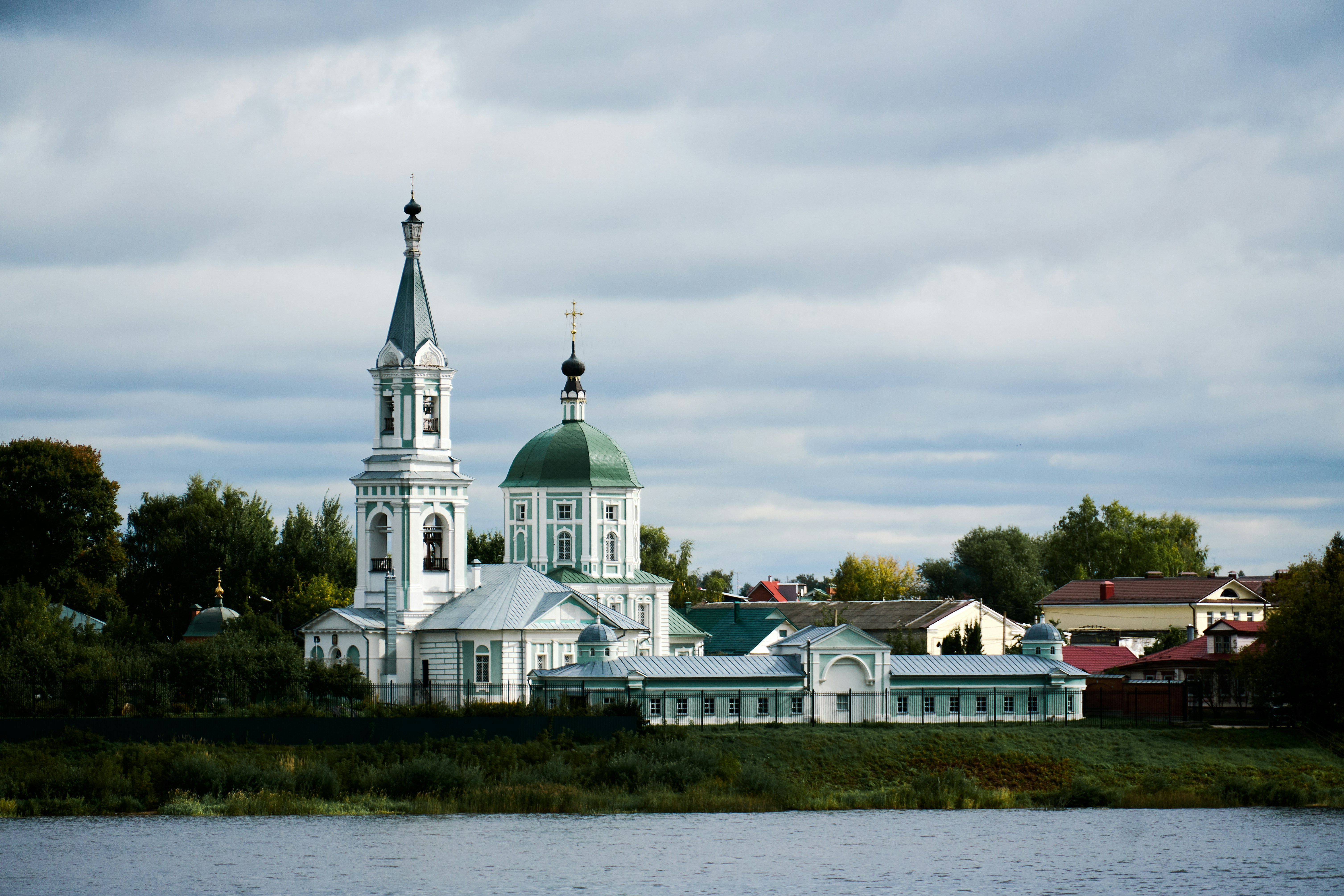An Orthodox church with a green dome and bell tower beside a river