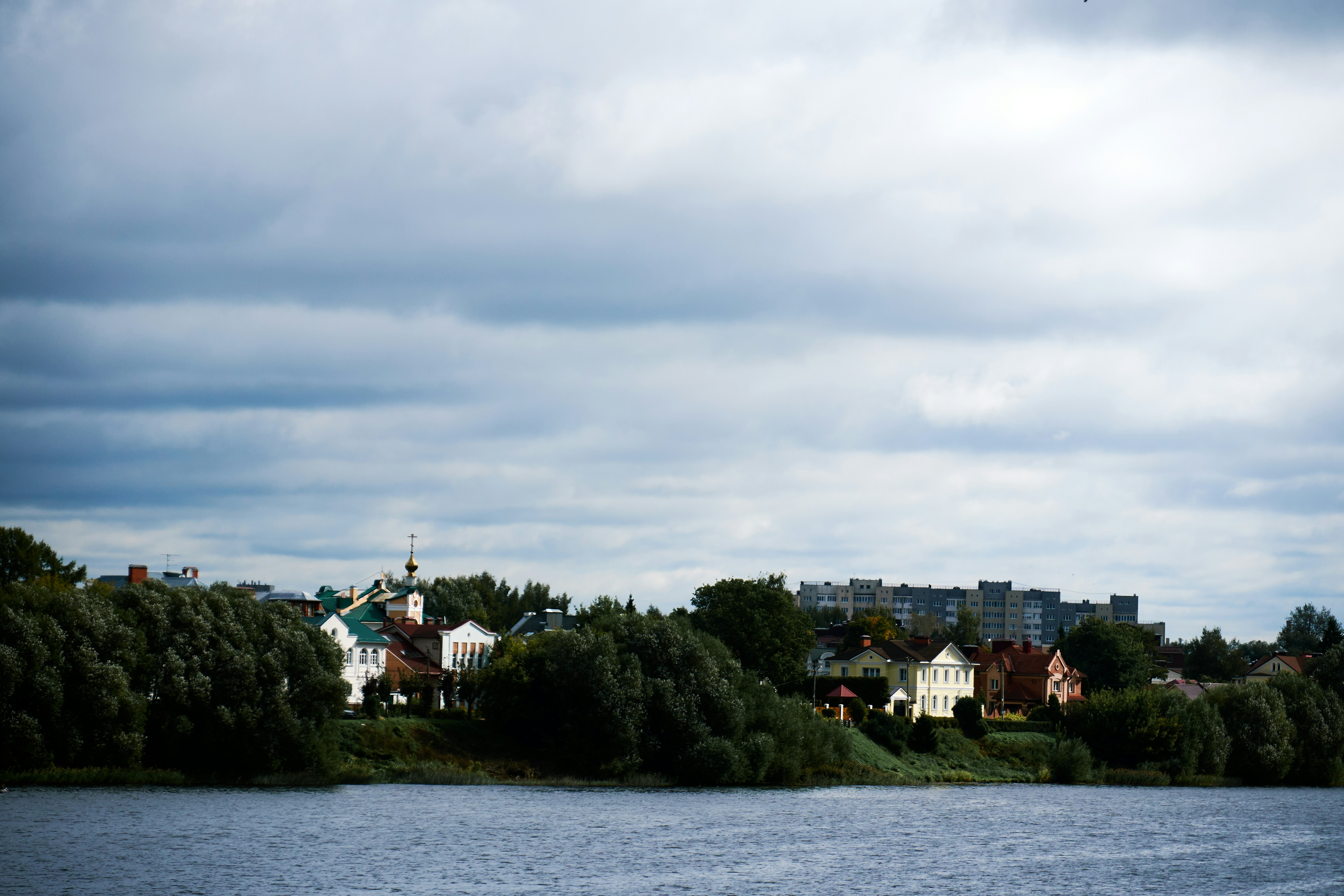 Houses and a church with a golden dome along a tree-lined riverbank
