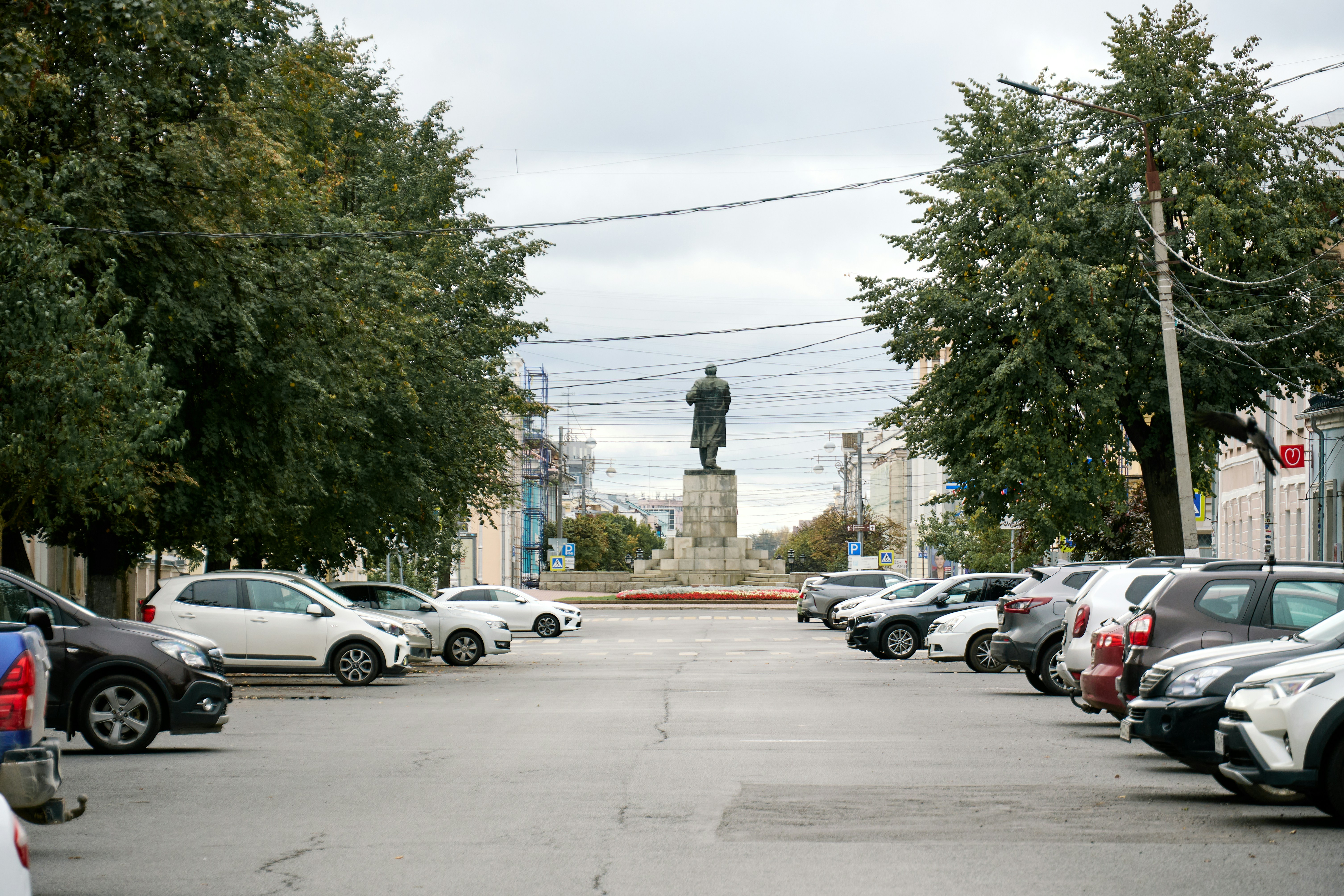 A bronze statue on a stone pedestal at the end of a parking lot