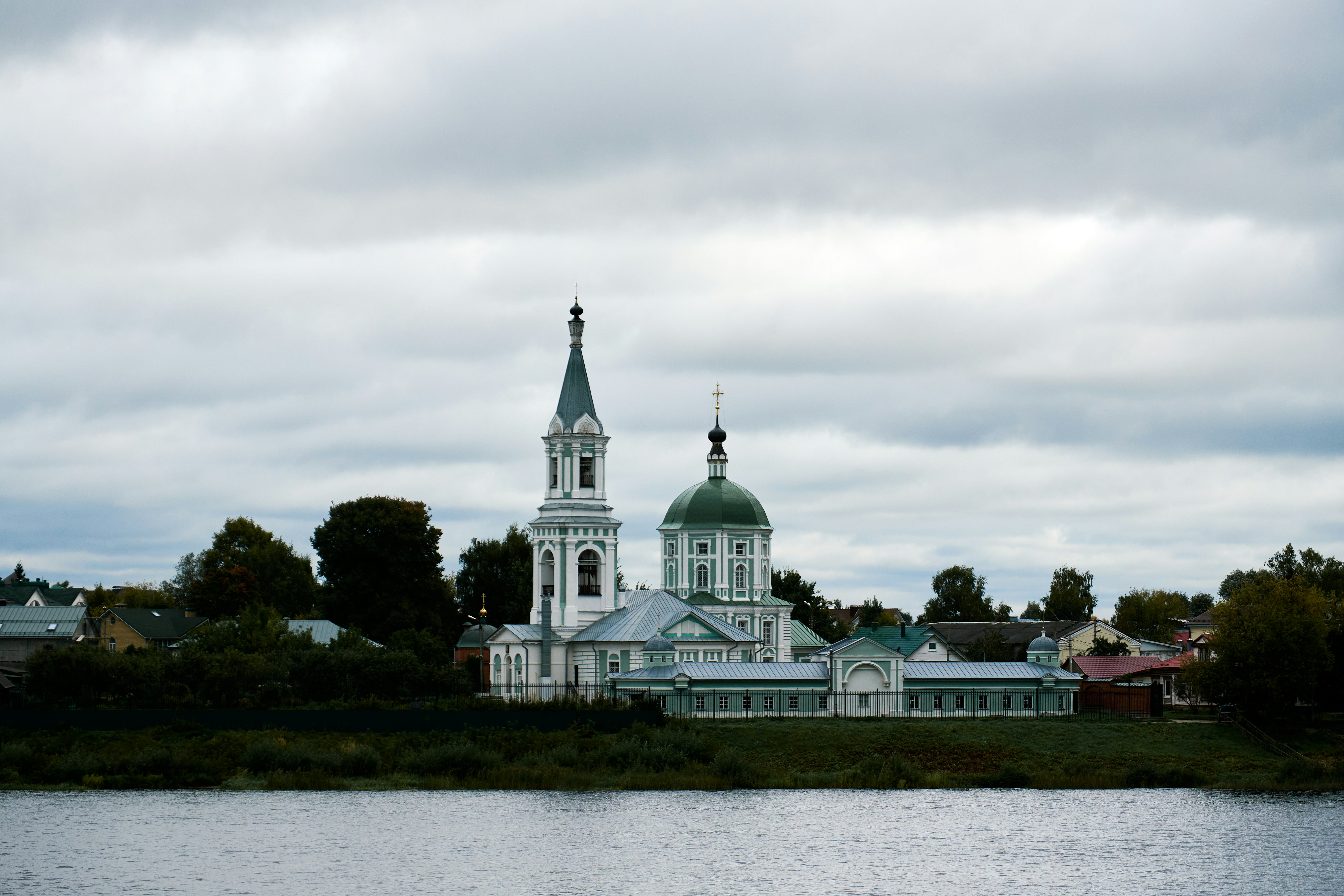 An Orthodox church with a green dome and bell tower beside a river