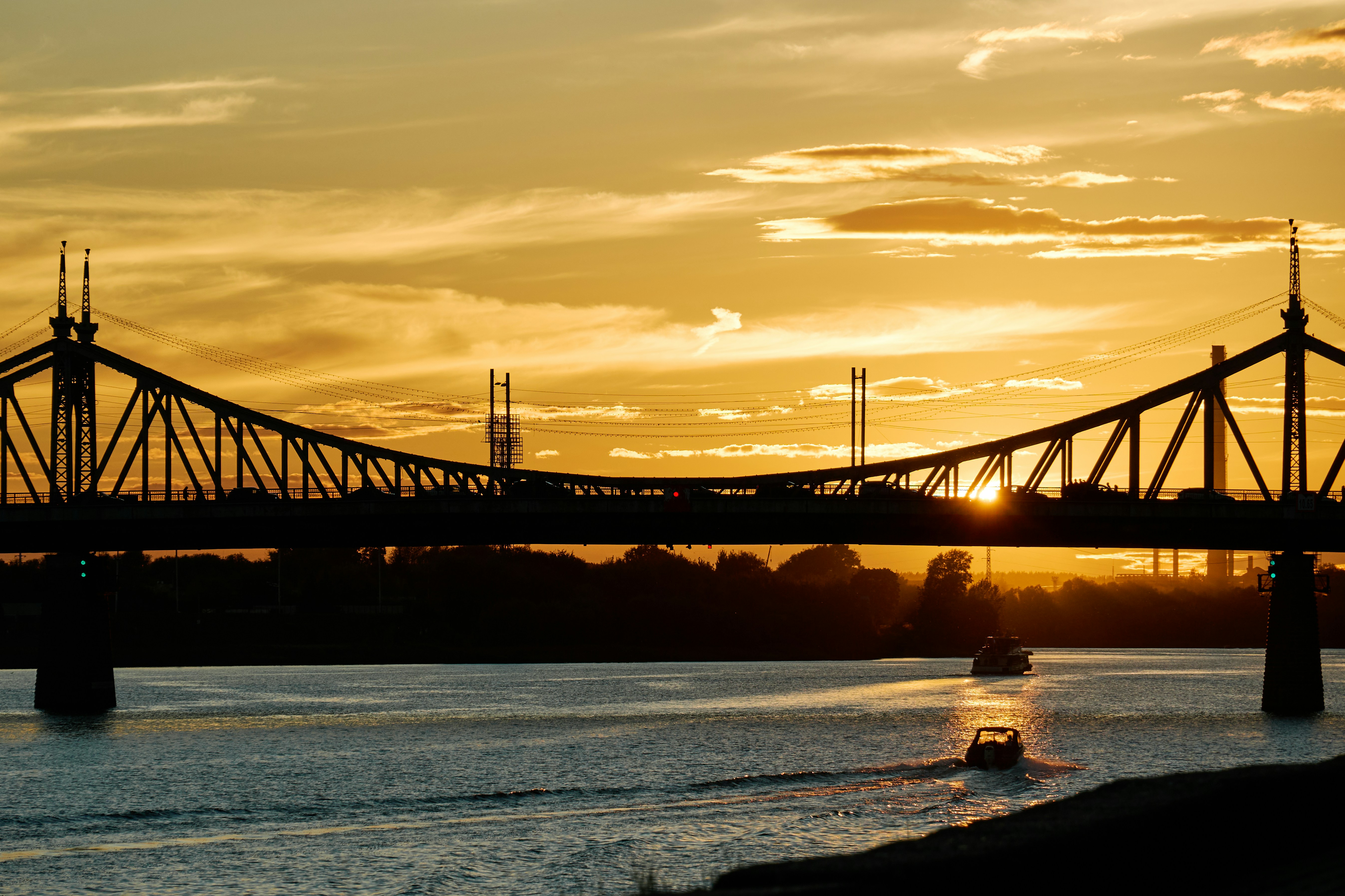 A bridge silhouette against a warm orange sky with a boat on the river