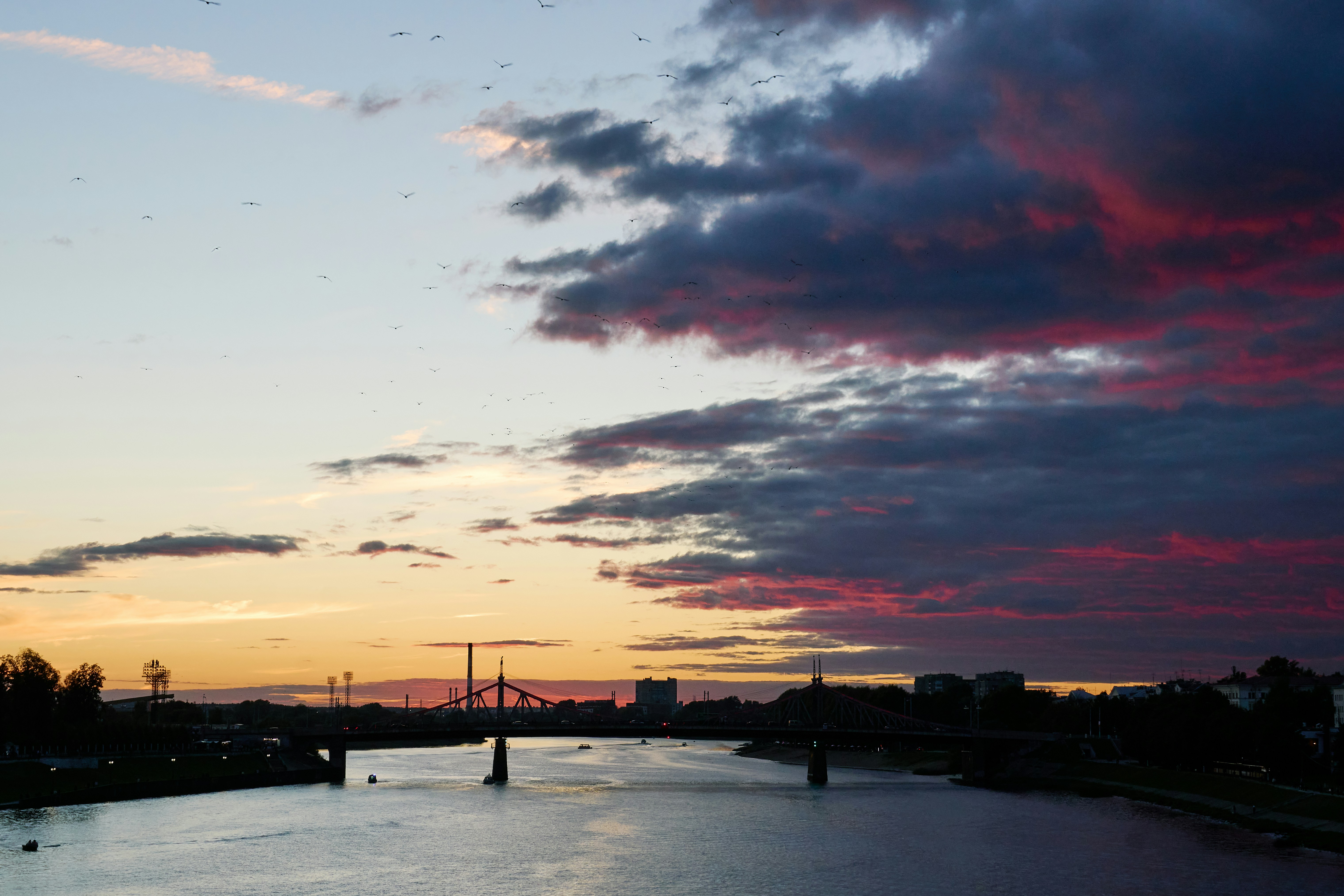 A bridge over a river under a sky with pink and dark clouds