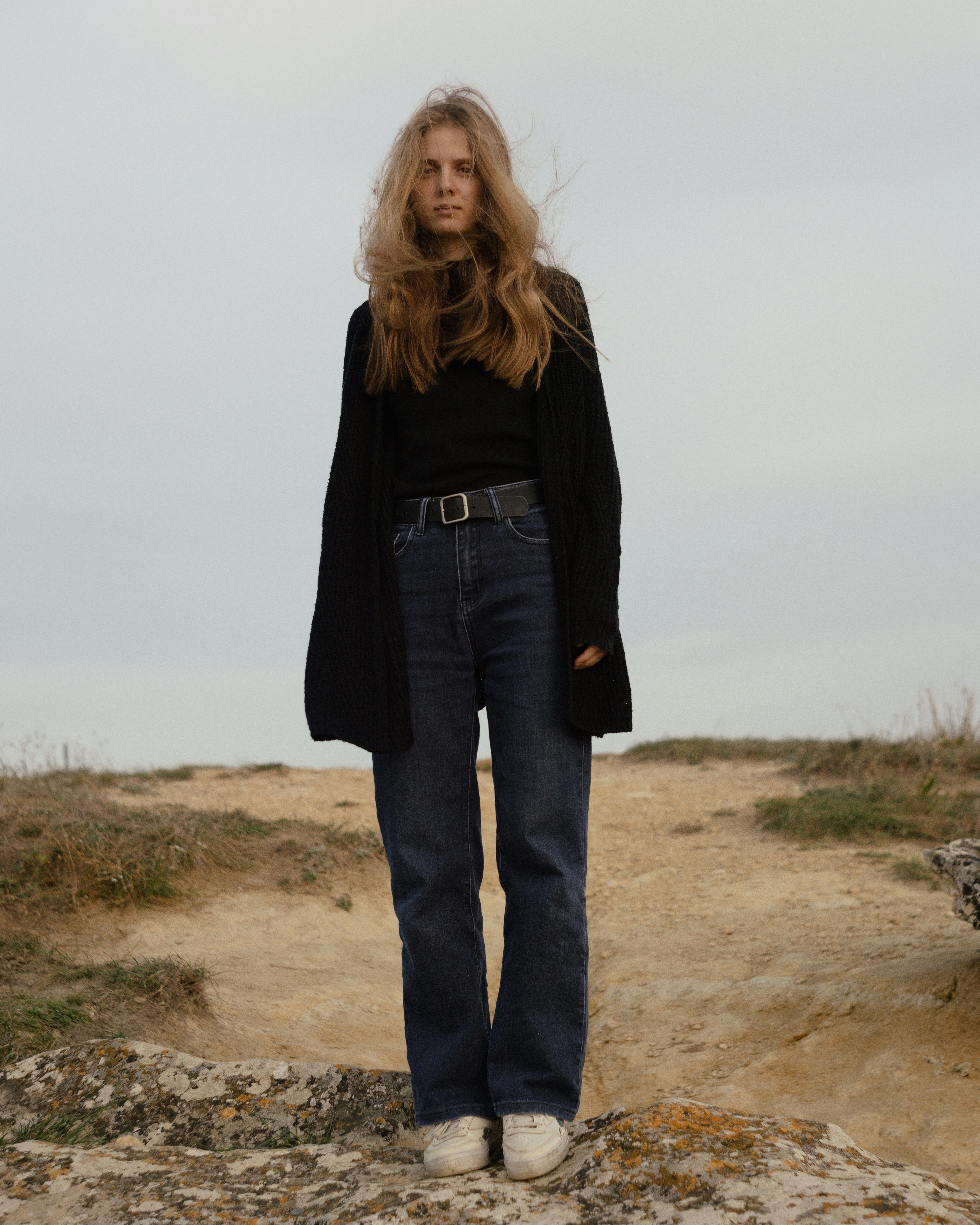 A woman in a black cardigan and blue jeans on a rocky outcrop