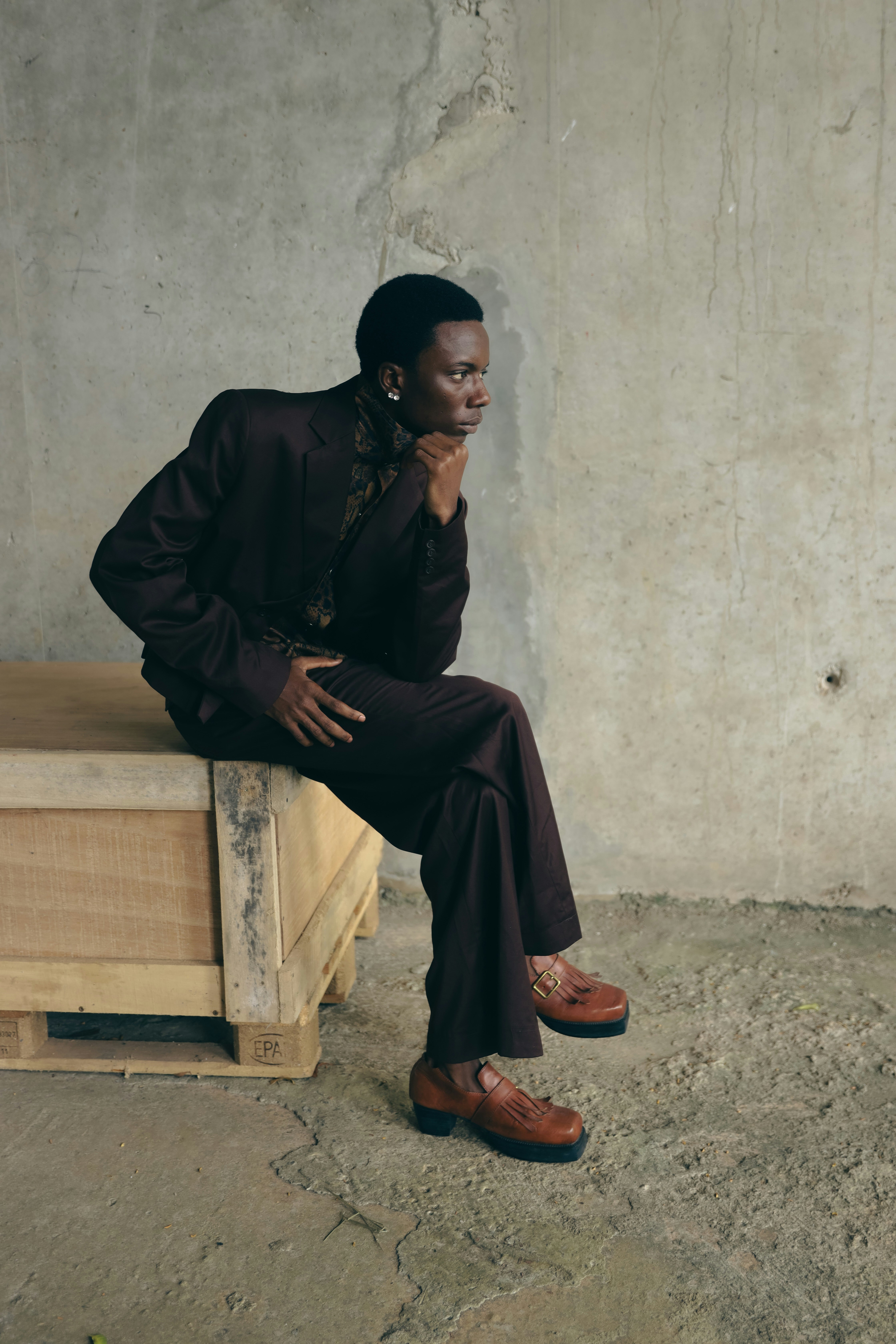 A man in a dark brown suit sitting on a wooden crate