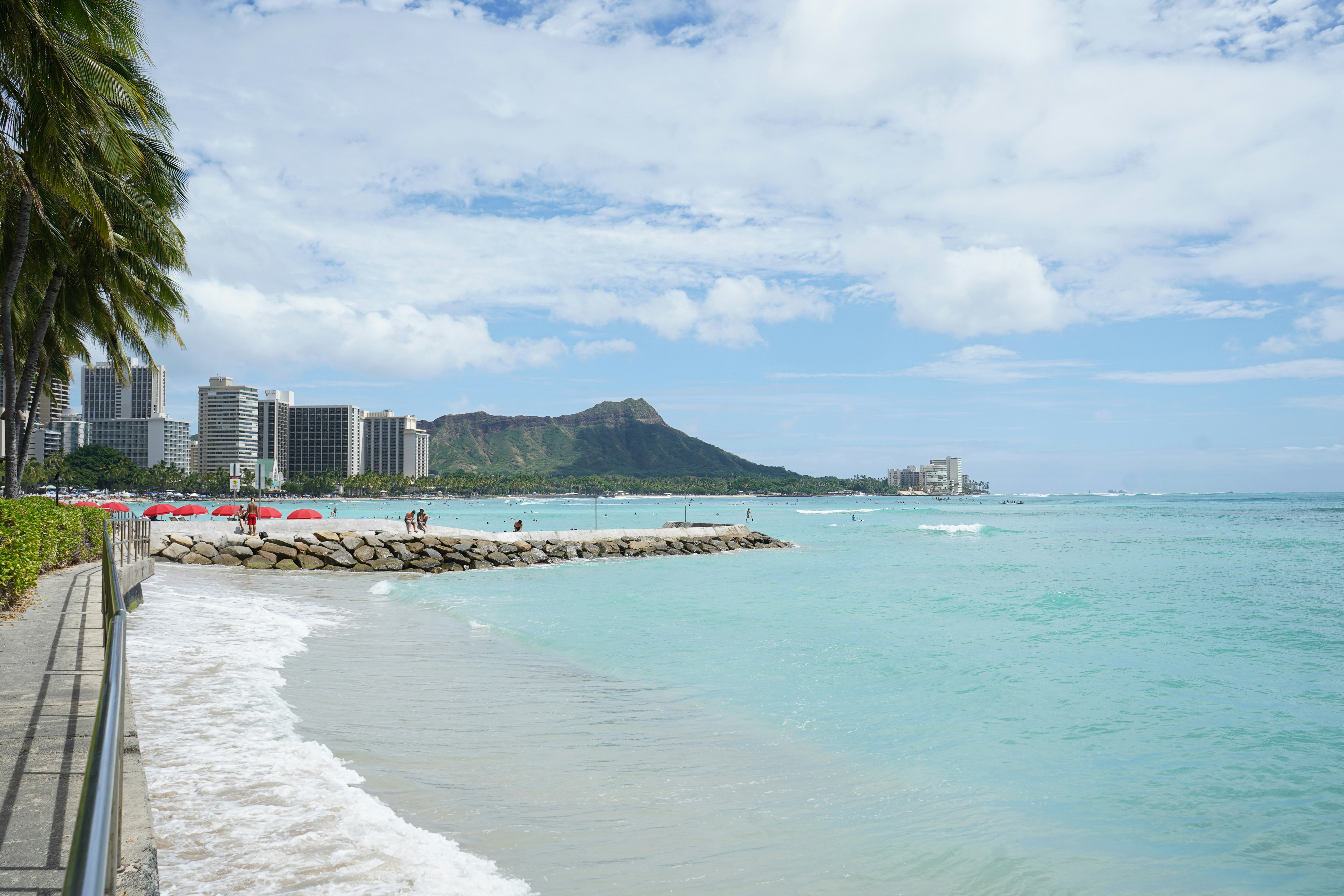 A rocky breakwater extending into turquoise water with Diamond Head and Honolulu skyline