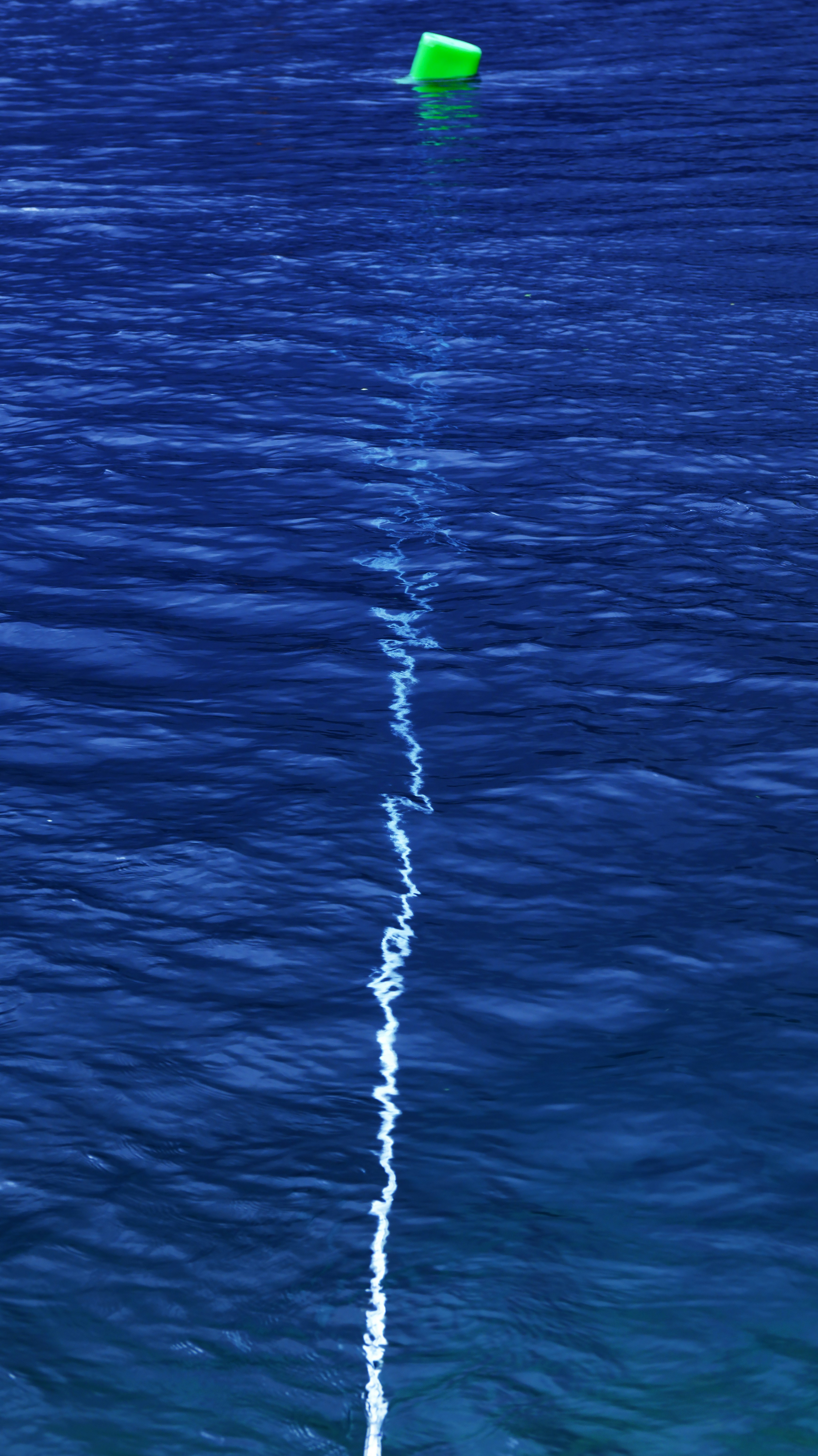 A bright green buoy floating on deep blue water with a white line