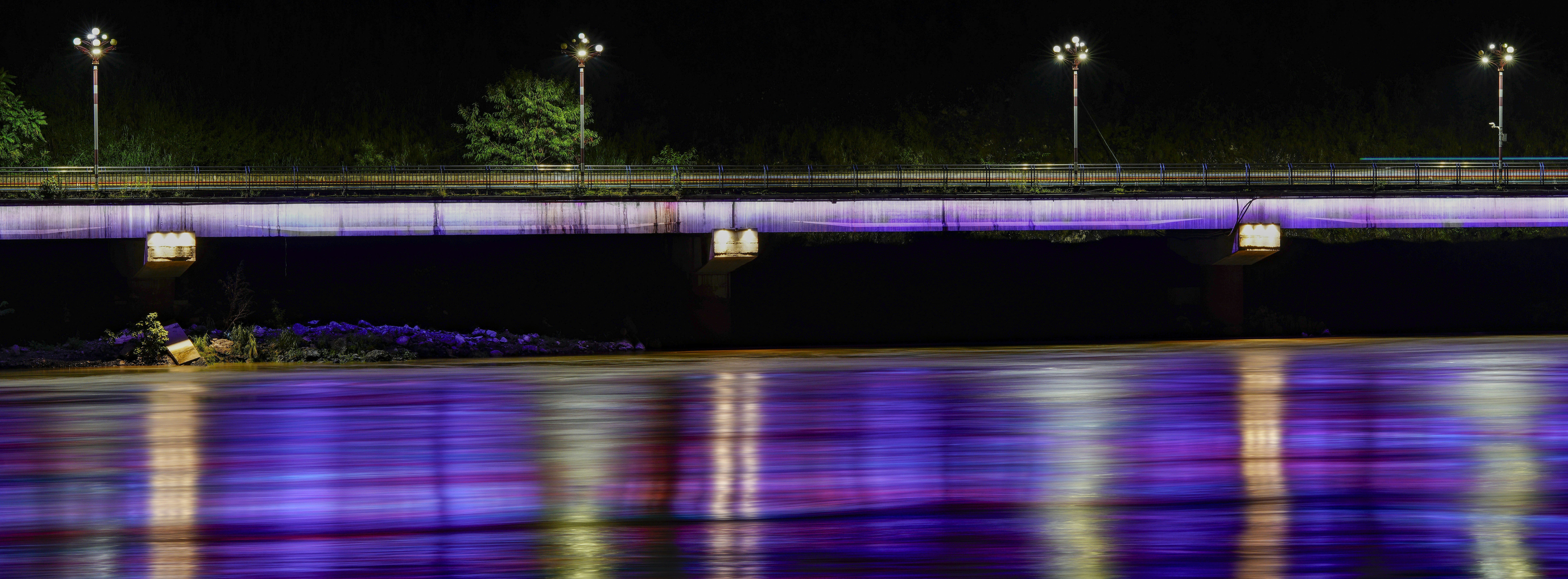 A long exposure of a bridge with purple lights reflecting on a river