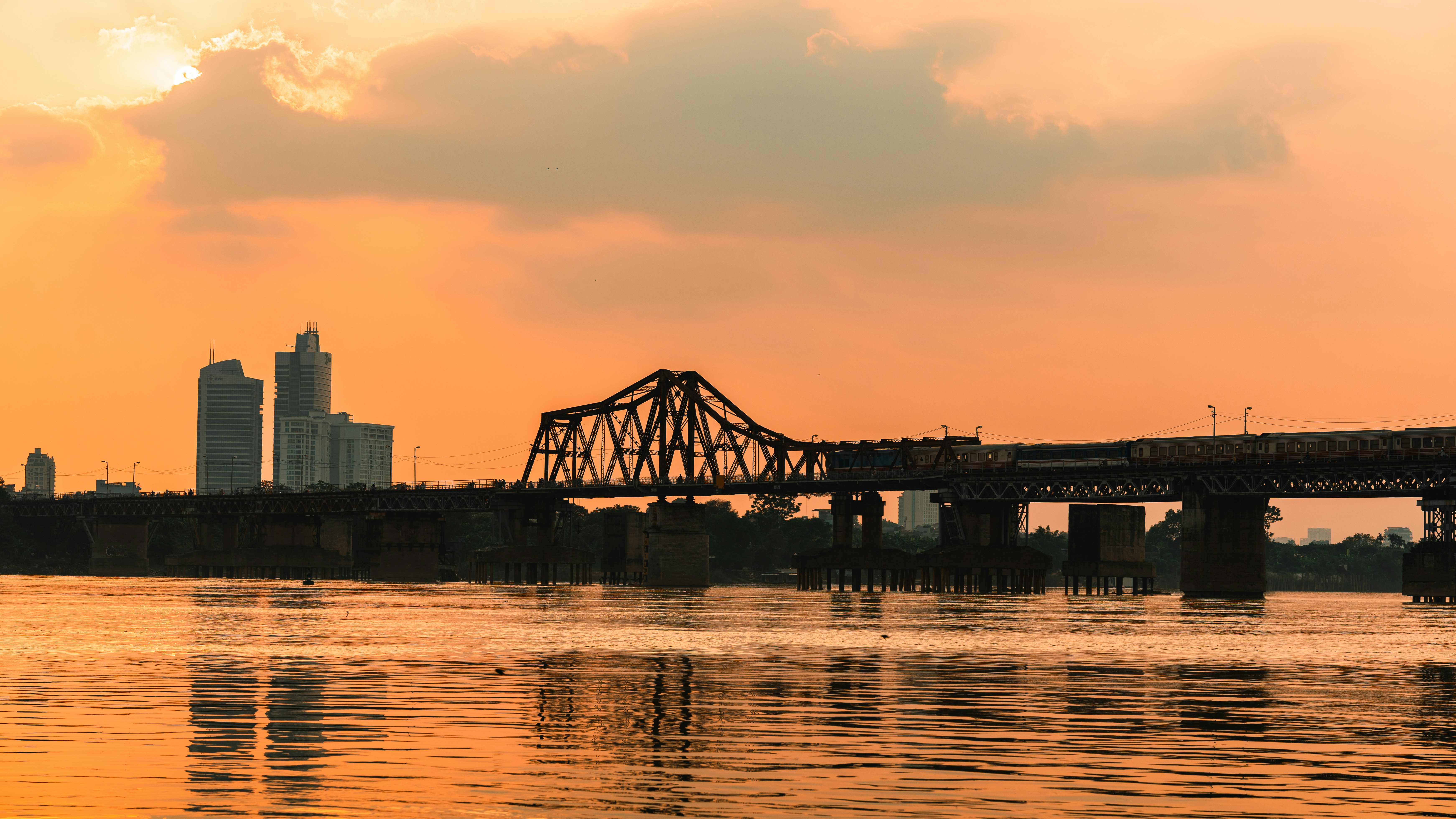 A train crossing the Long Bien Bridge over a river at golden hour