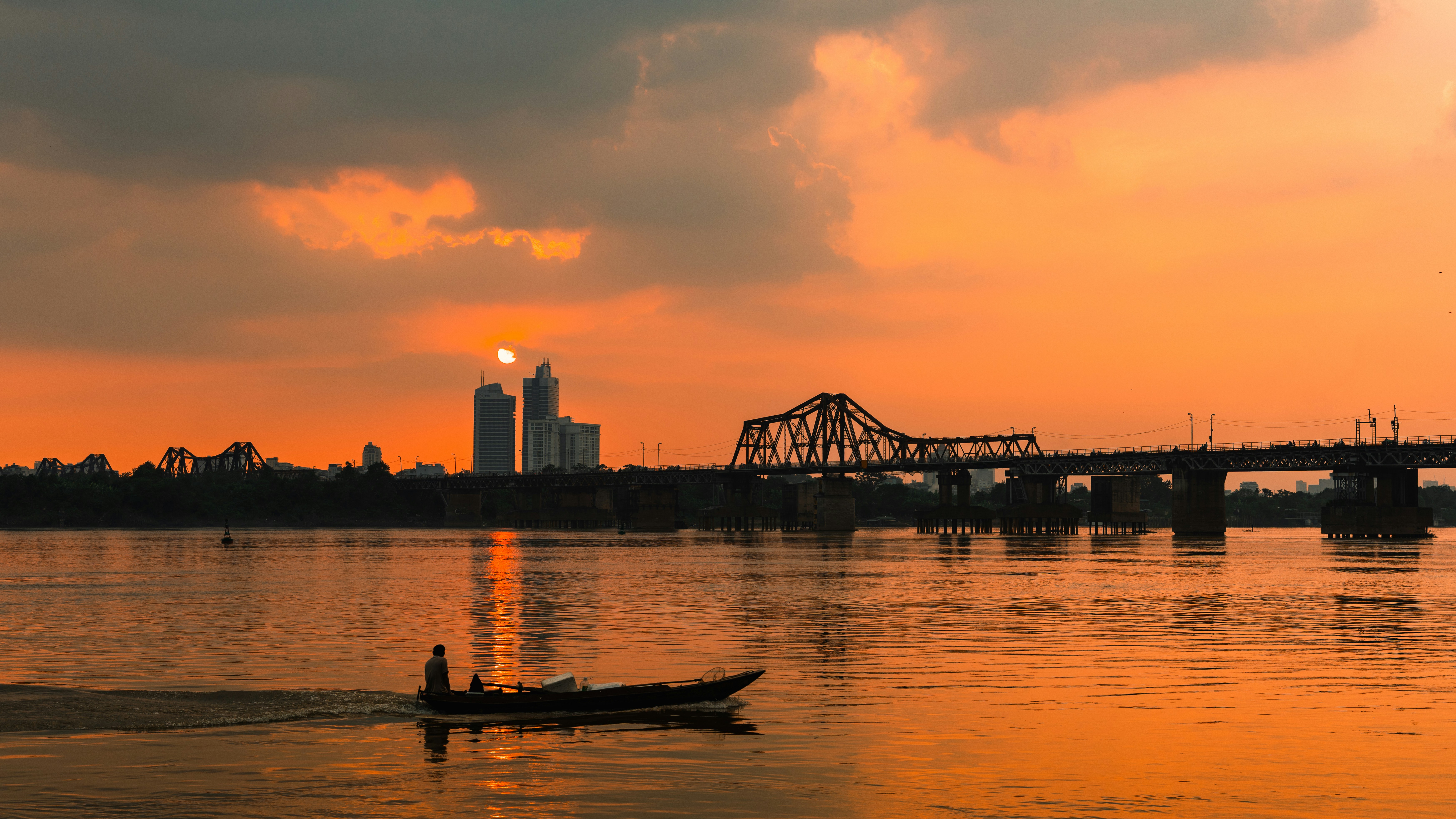 A person in a small boat on a river under a warm orange sky