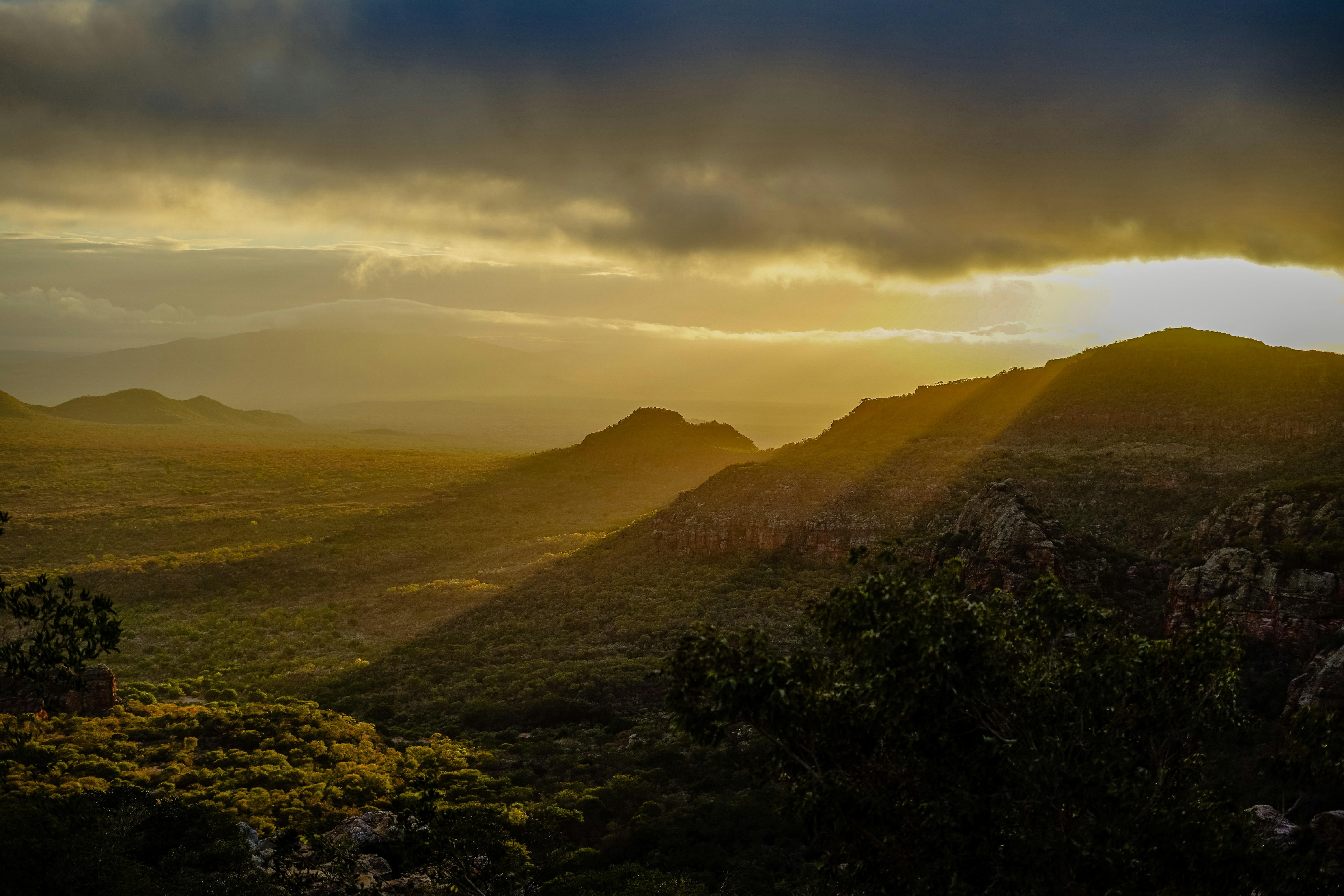 Low sun casting long shadows over a vast valley with green hills