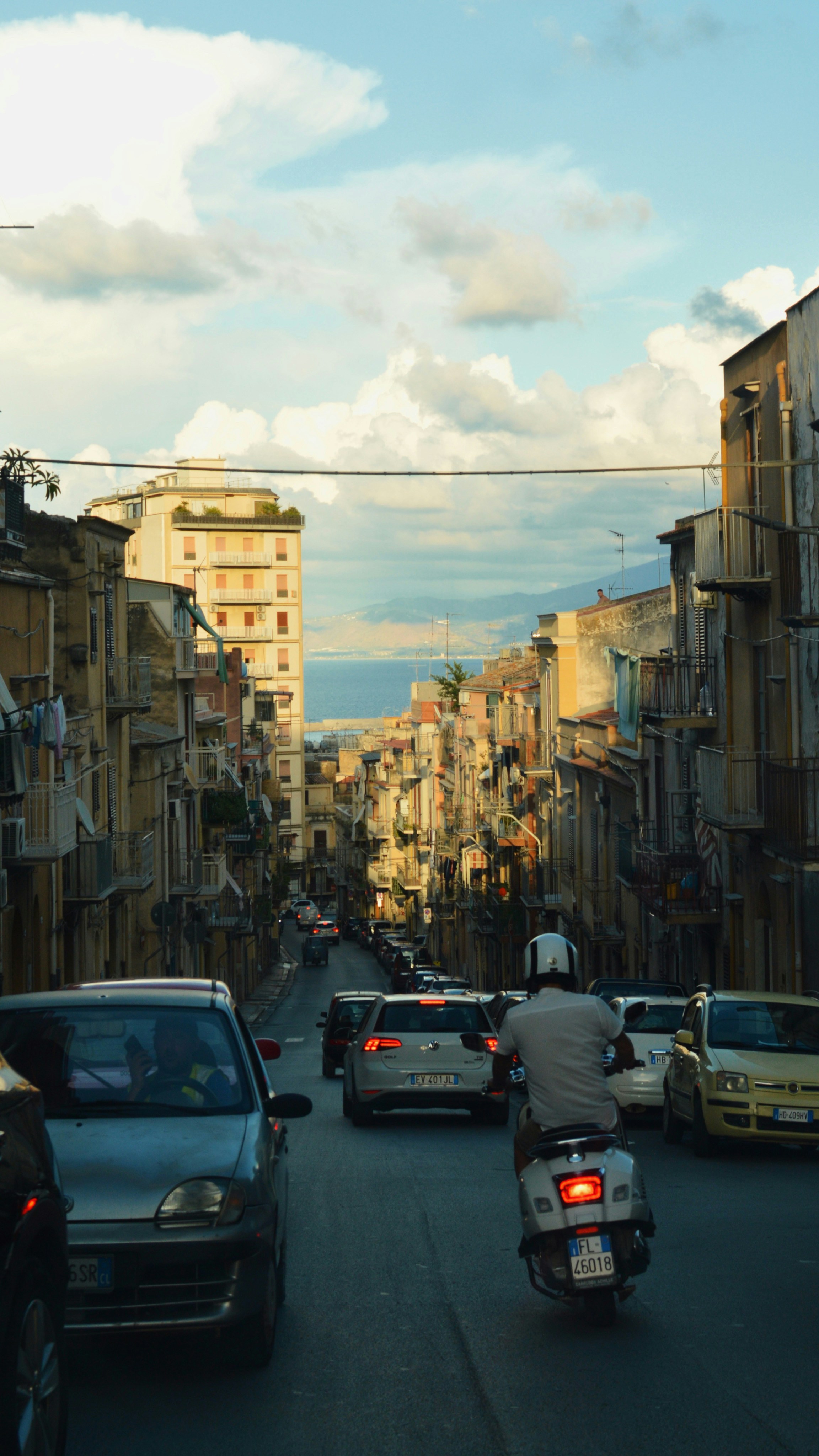 A person riding a scooter down a narrow street toward the sea
