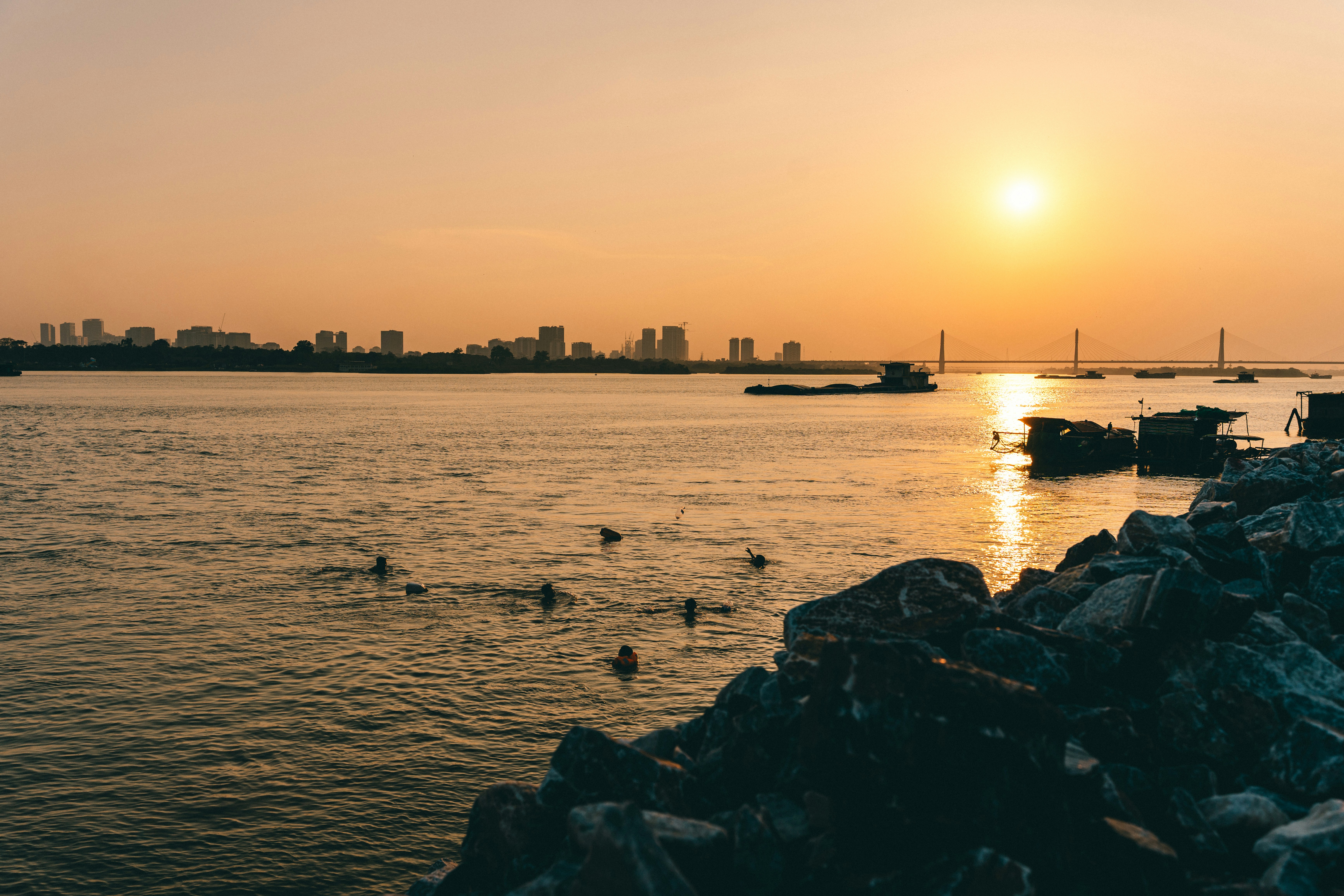 People swimming in a river near a rocky bank during the golden hour