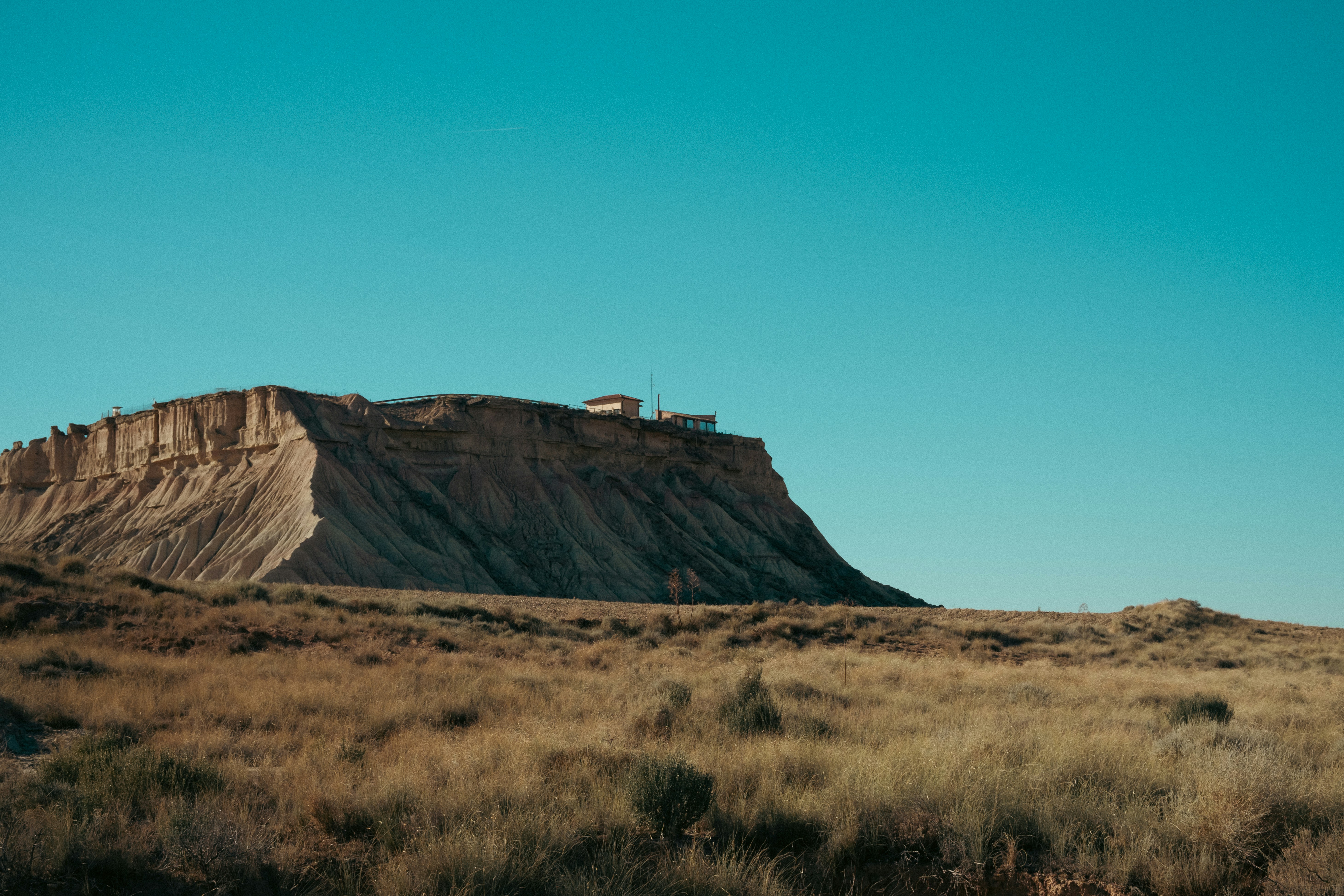 A small building on a rocky cliff above a dry grassy landscape