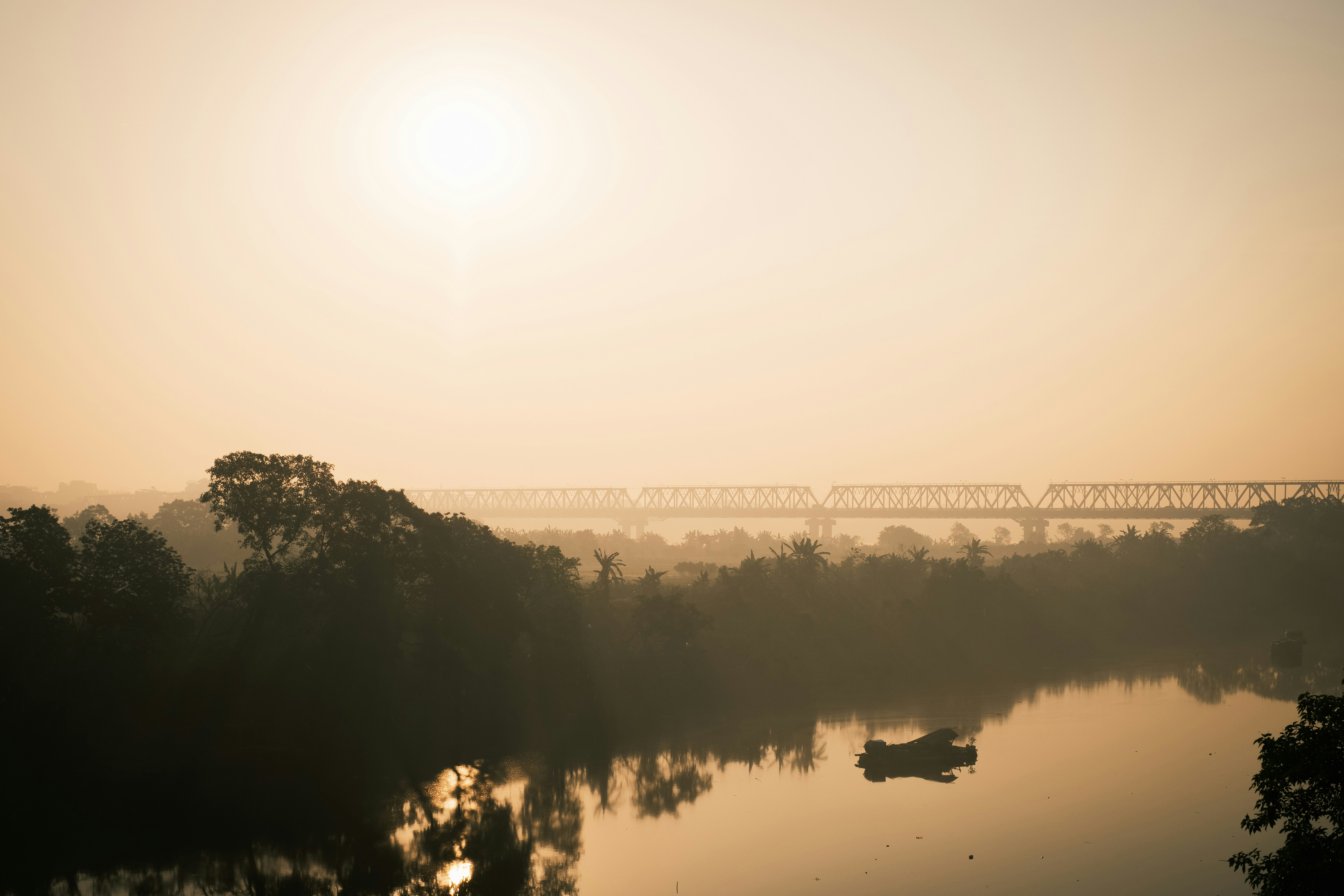 A railway bridge crossing a river under a hazy golden sky