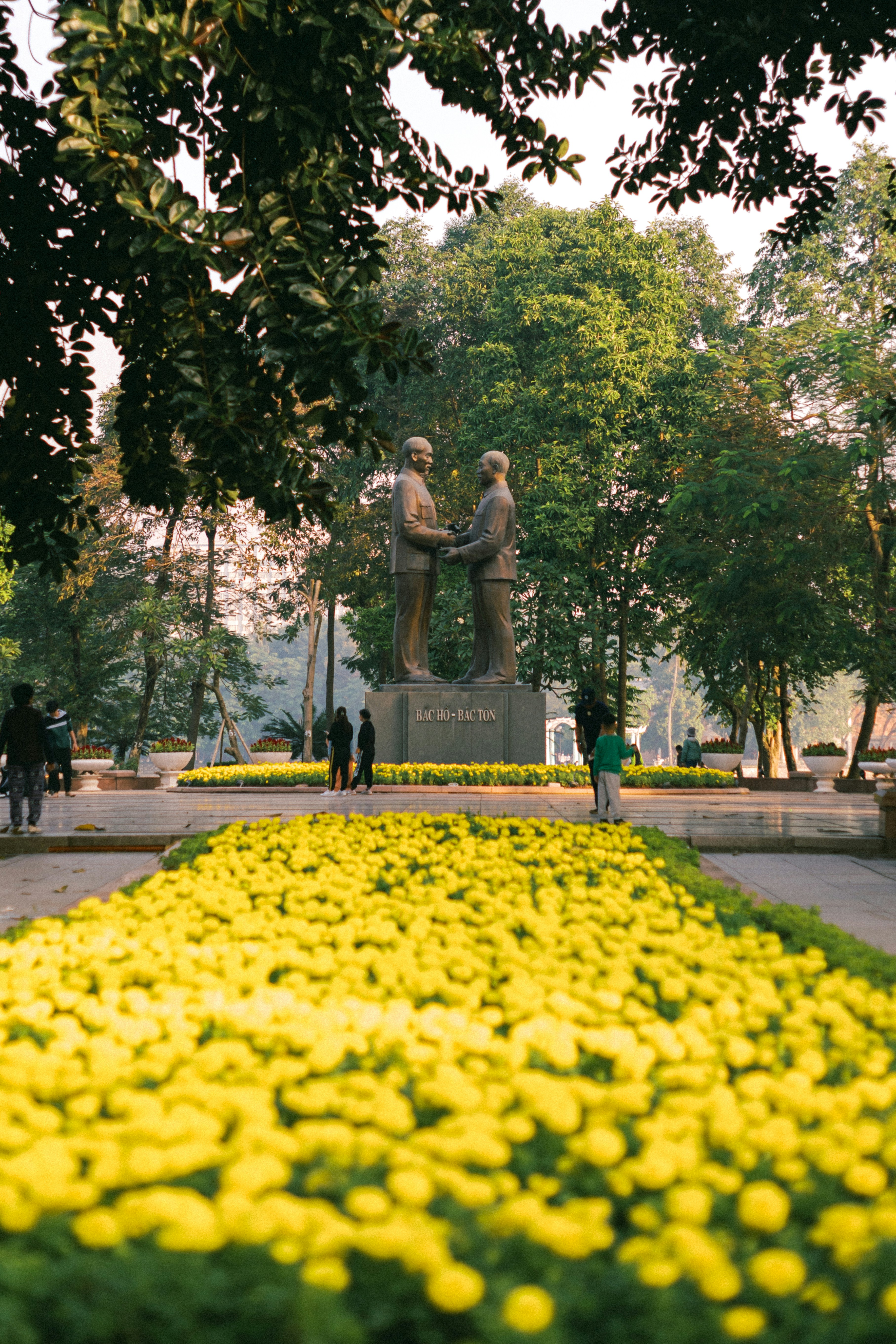 A bronze statue of two men shaking hands in a park with yellow flowers