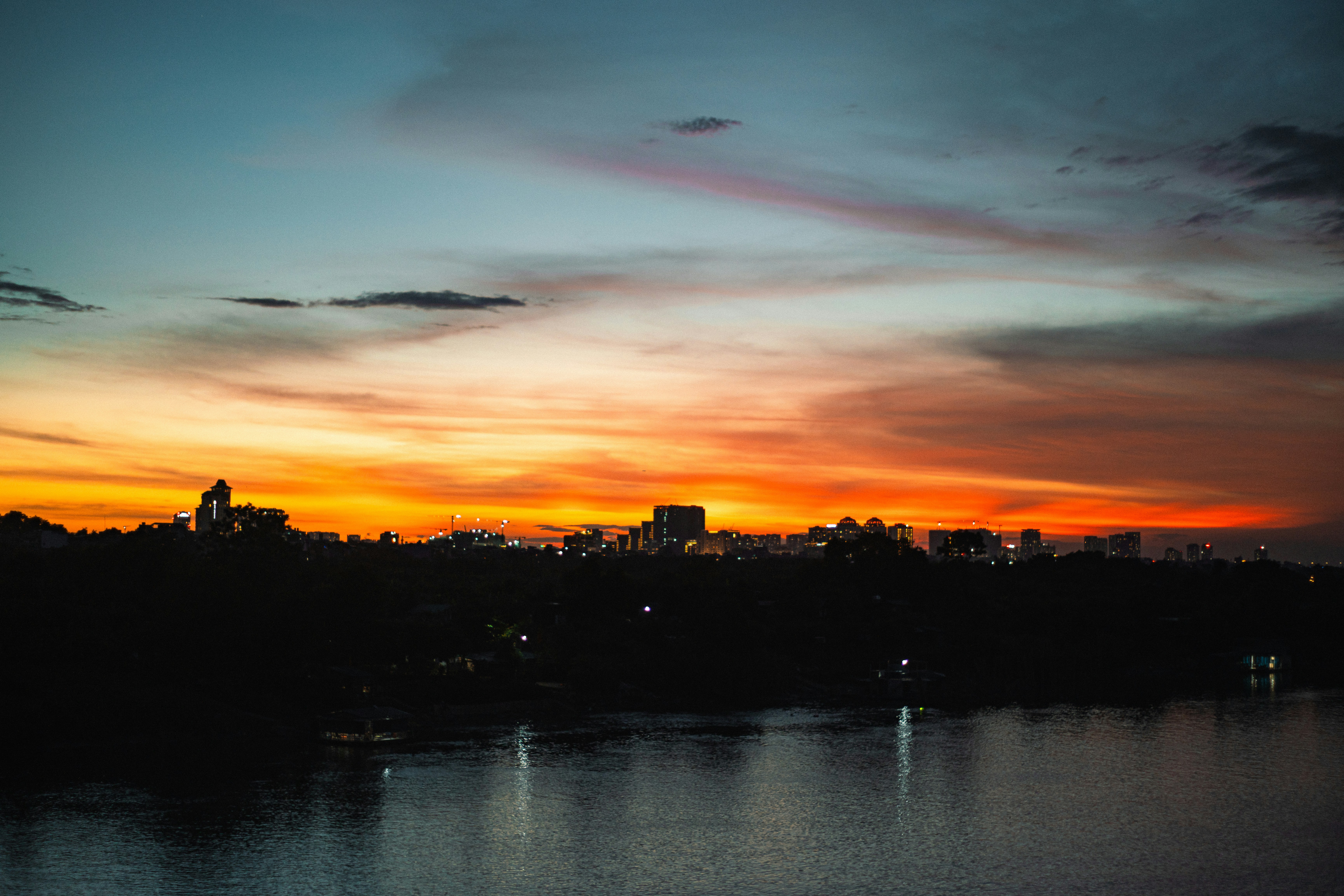 A city skyline silhouette against a vibrant orange and blue sky above water