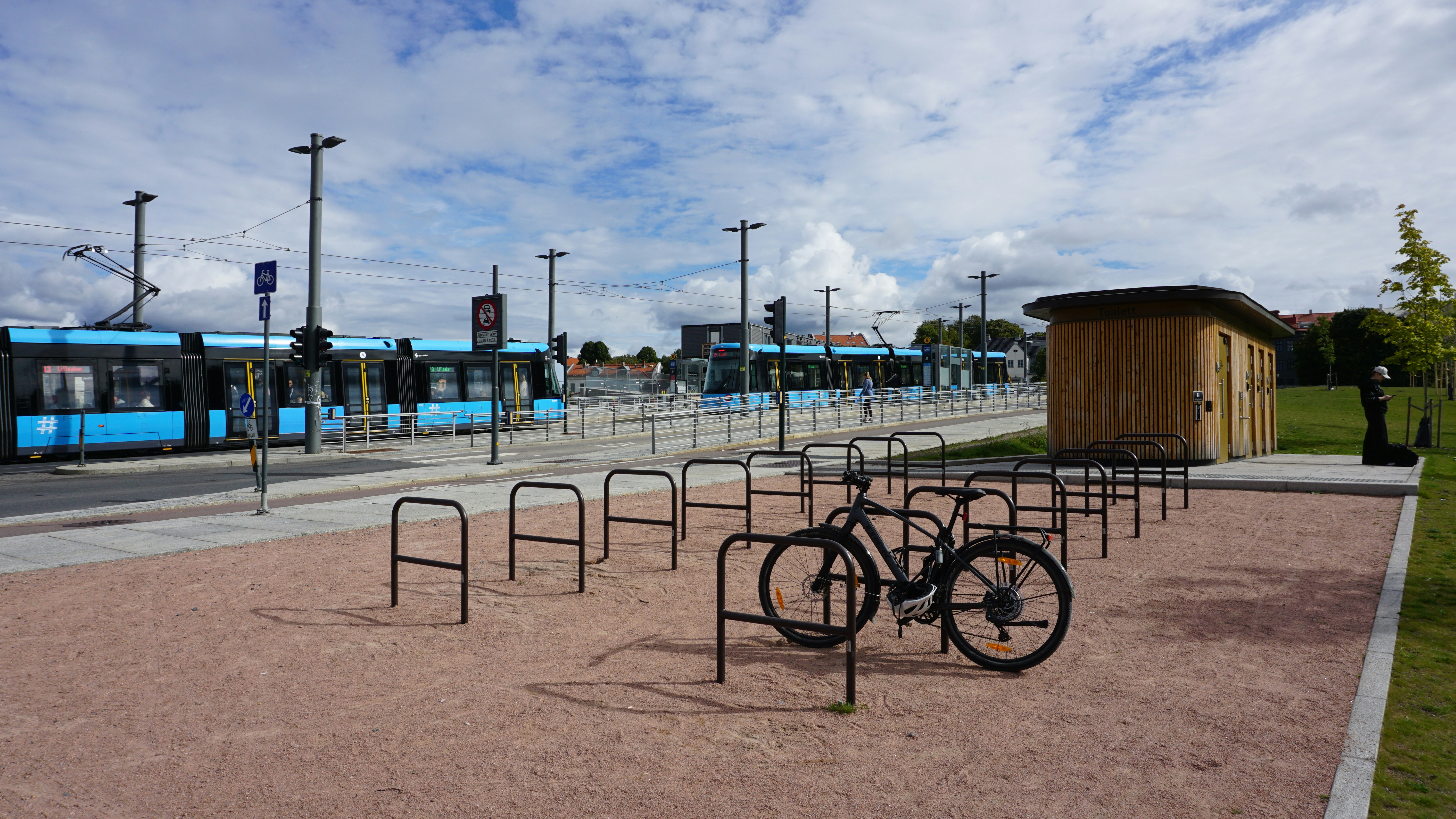 Una bicicleta aparcada en un portaequipajes metálico cerca de un tranvía azul sobre vías