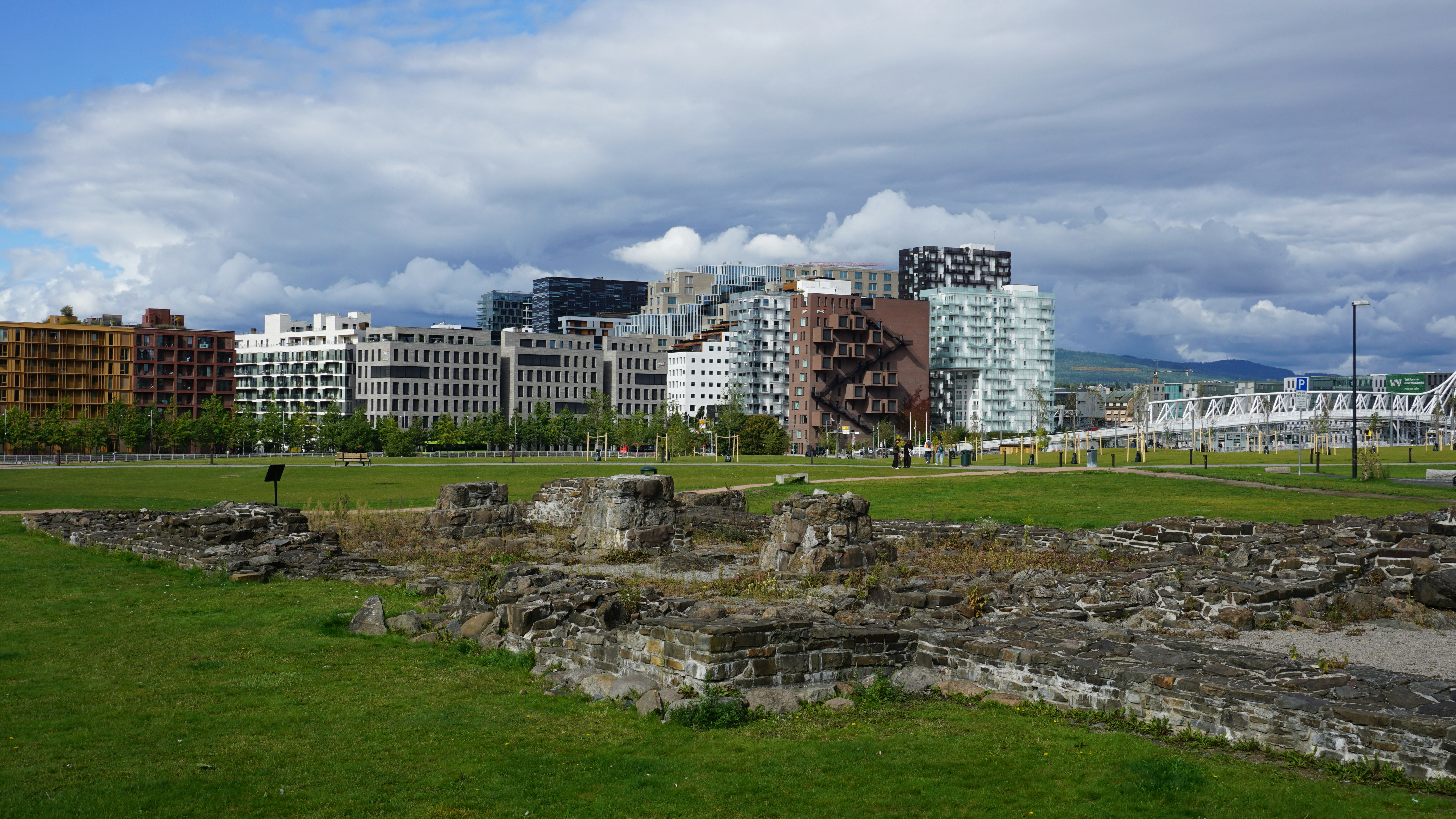 Stone ruins in a grassy park before a modern apartment skyline in Oslo