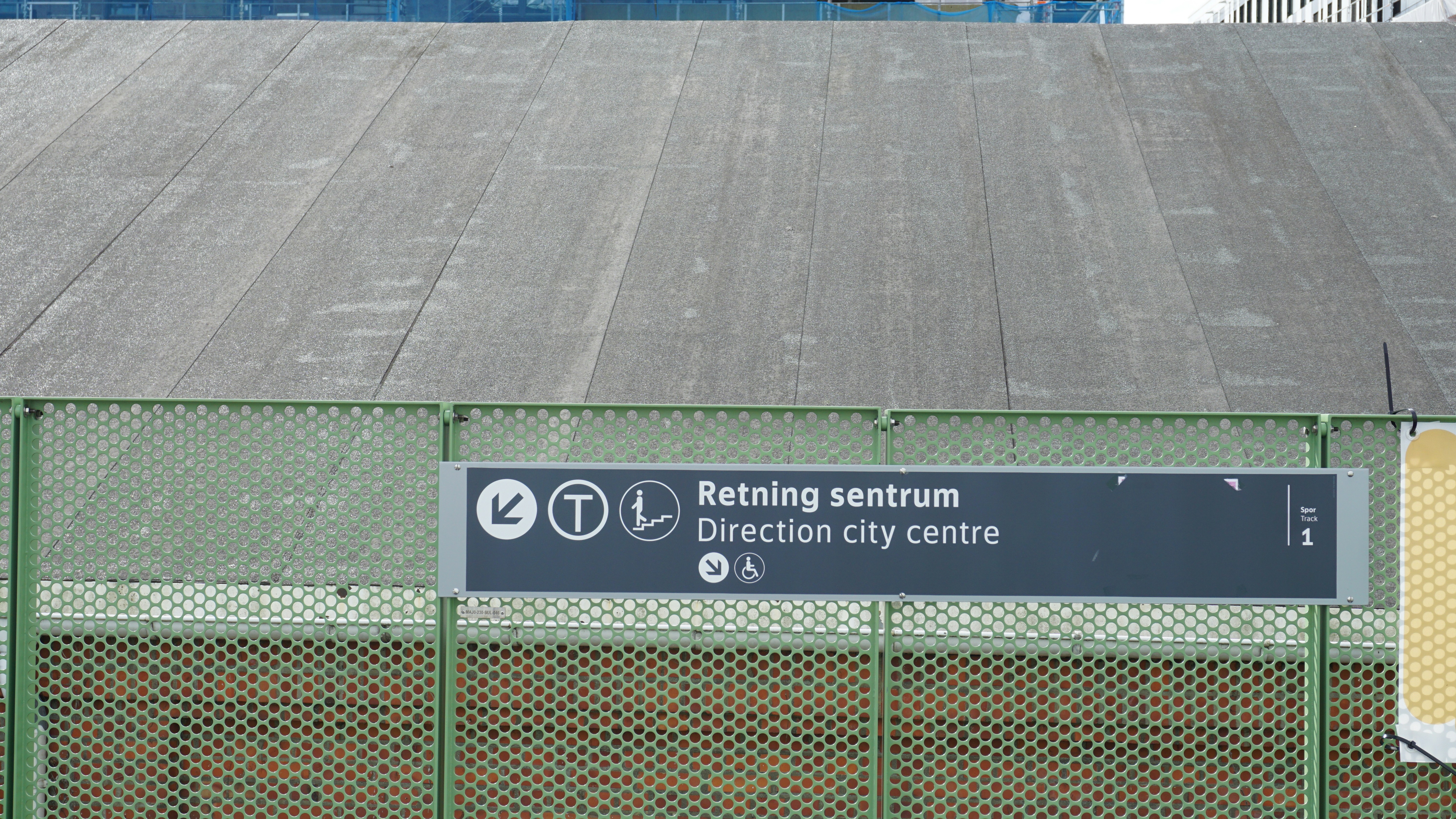 Un cartel direccional que dice Retning sentrum y Direction centro de la ciudad en una valla verde