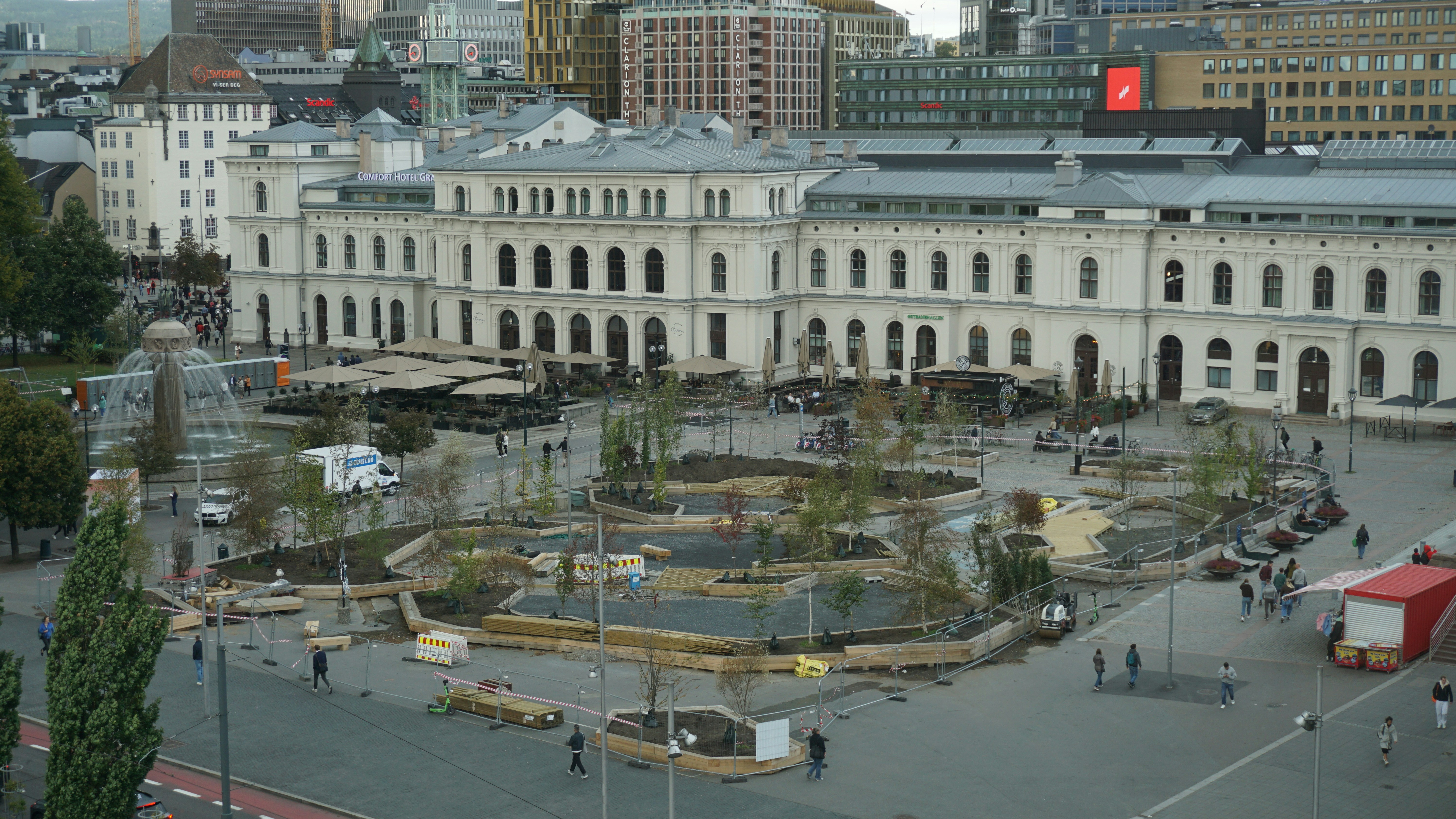 Gente paseando por una plaza de la ciudad con fuente y obras en Oslo
