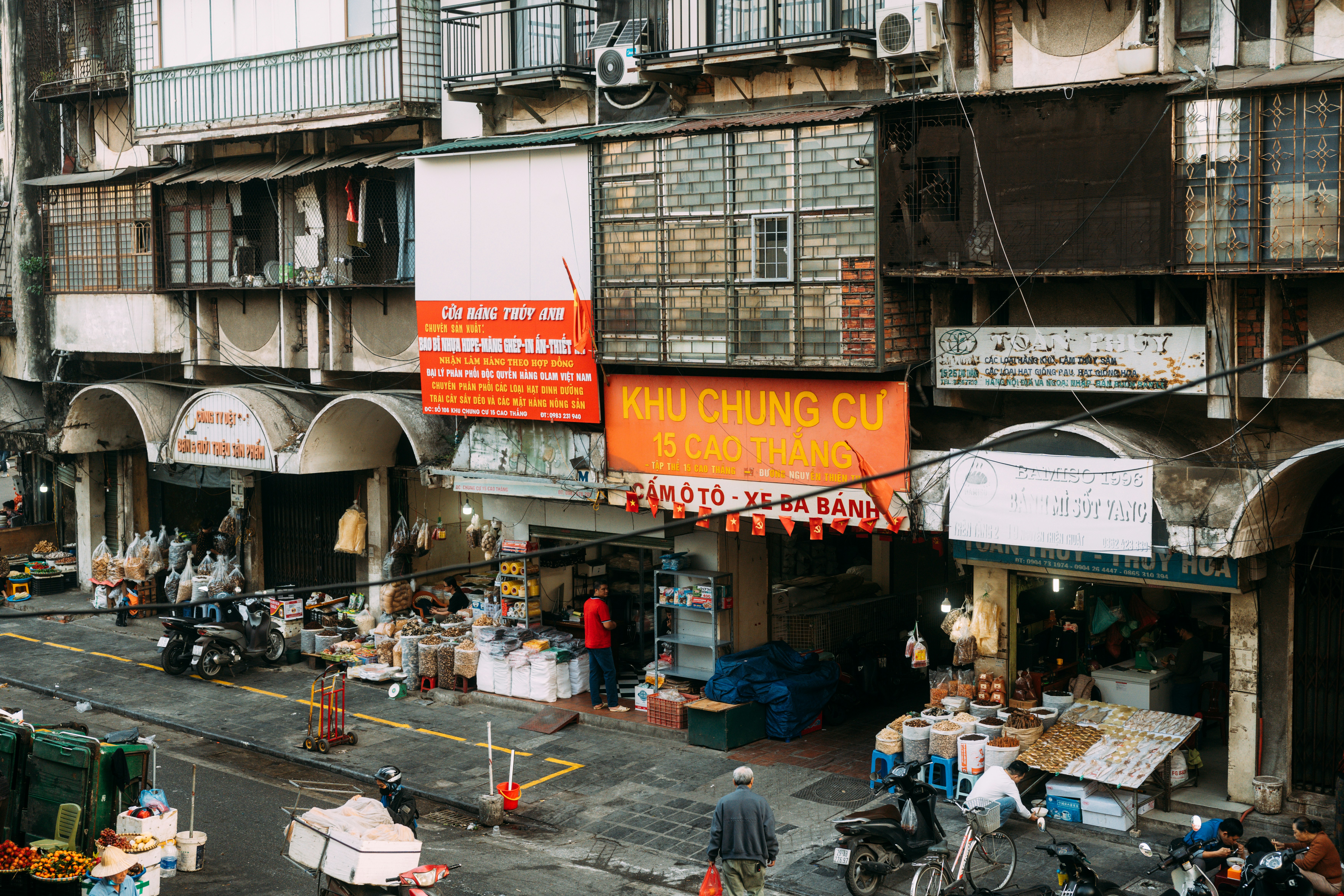 An elevated street view of open-front shops and market stalls below multi-story residential buildings