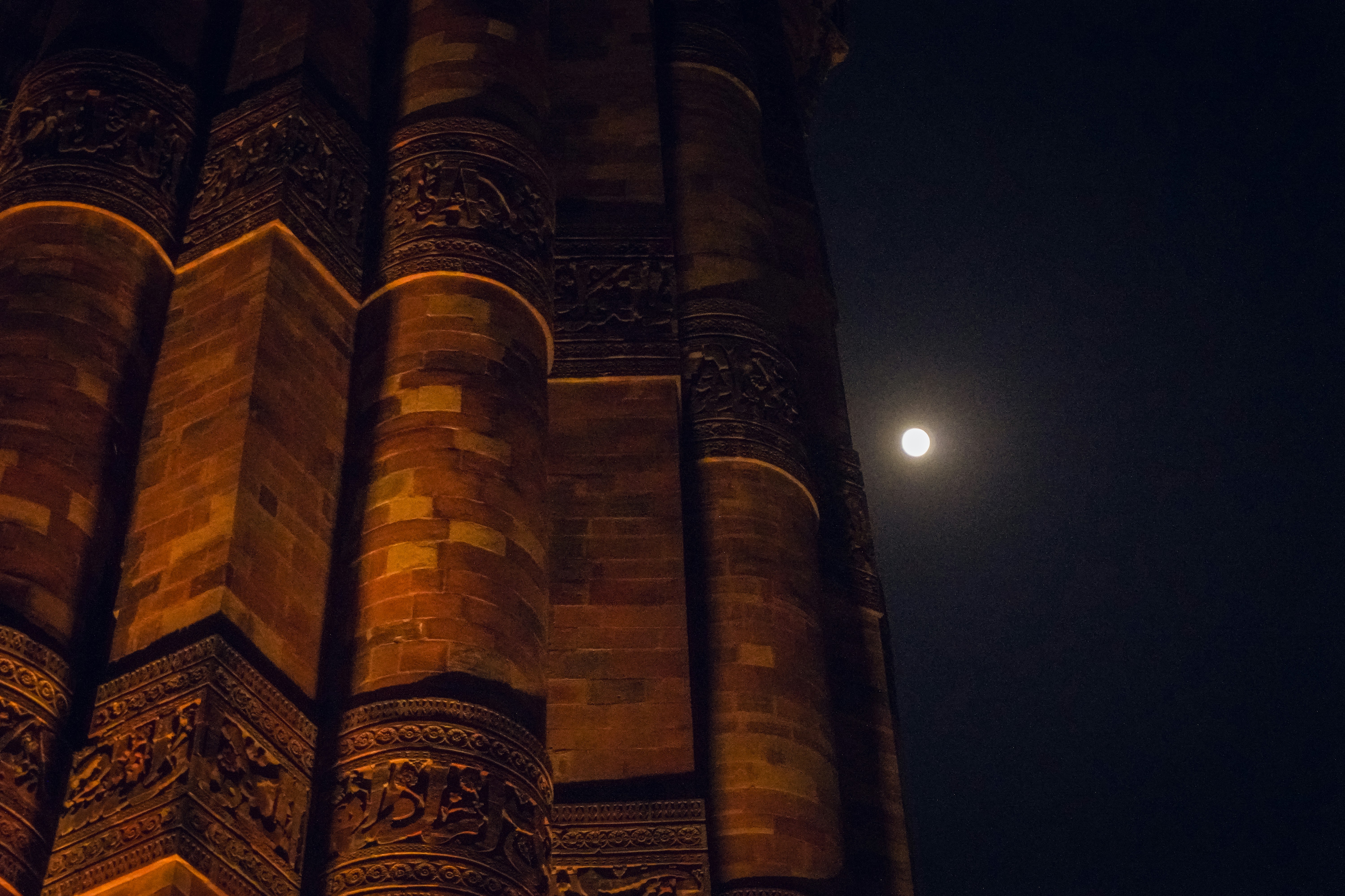 The Qutub Minar tower illuminated at night with a full moon in the sky