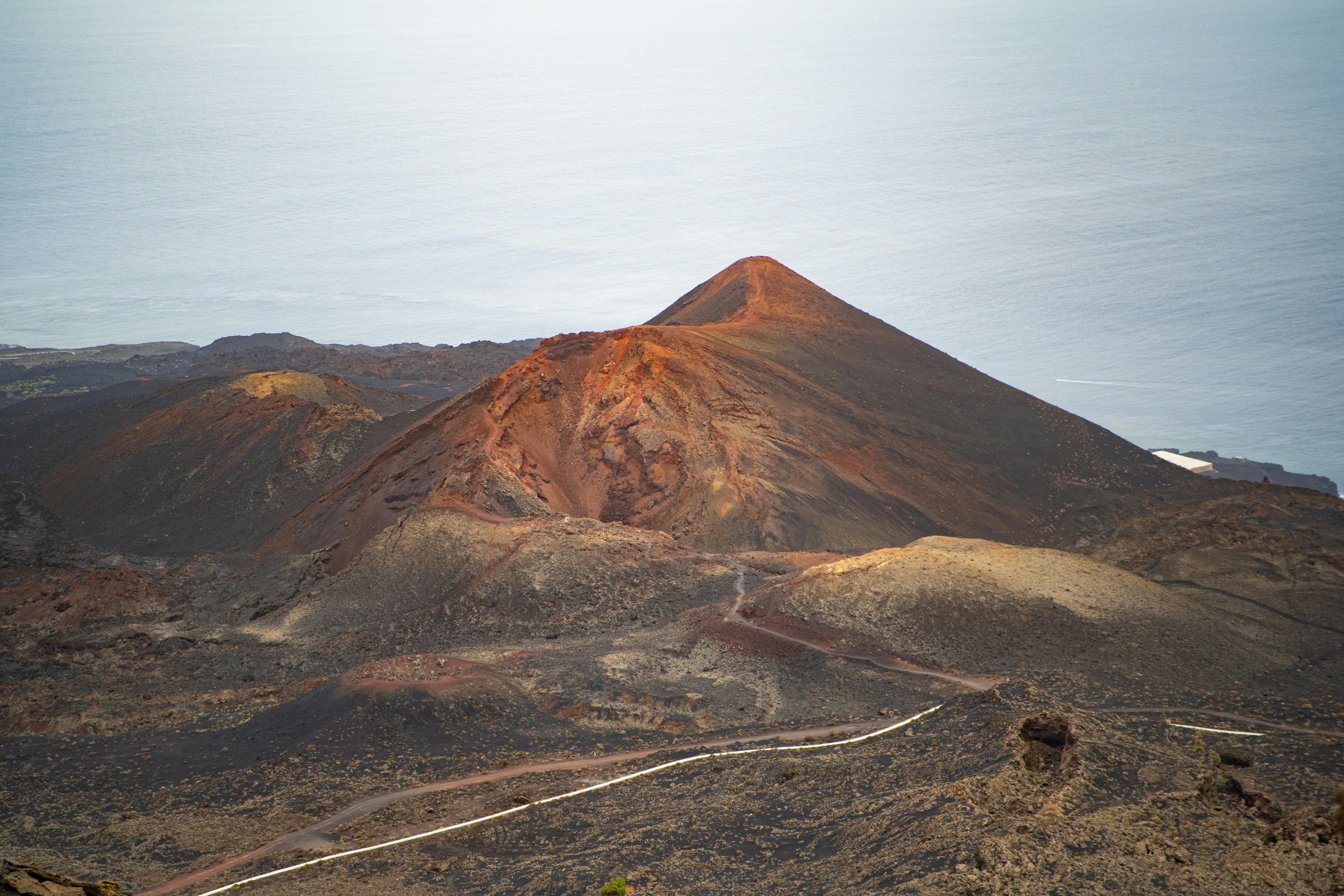 A volcanic crater with red and black rock above the blue ocean