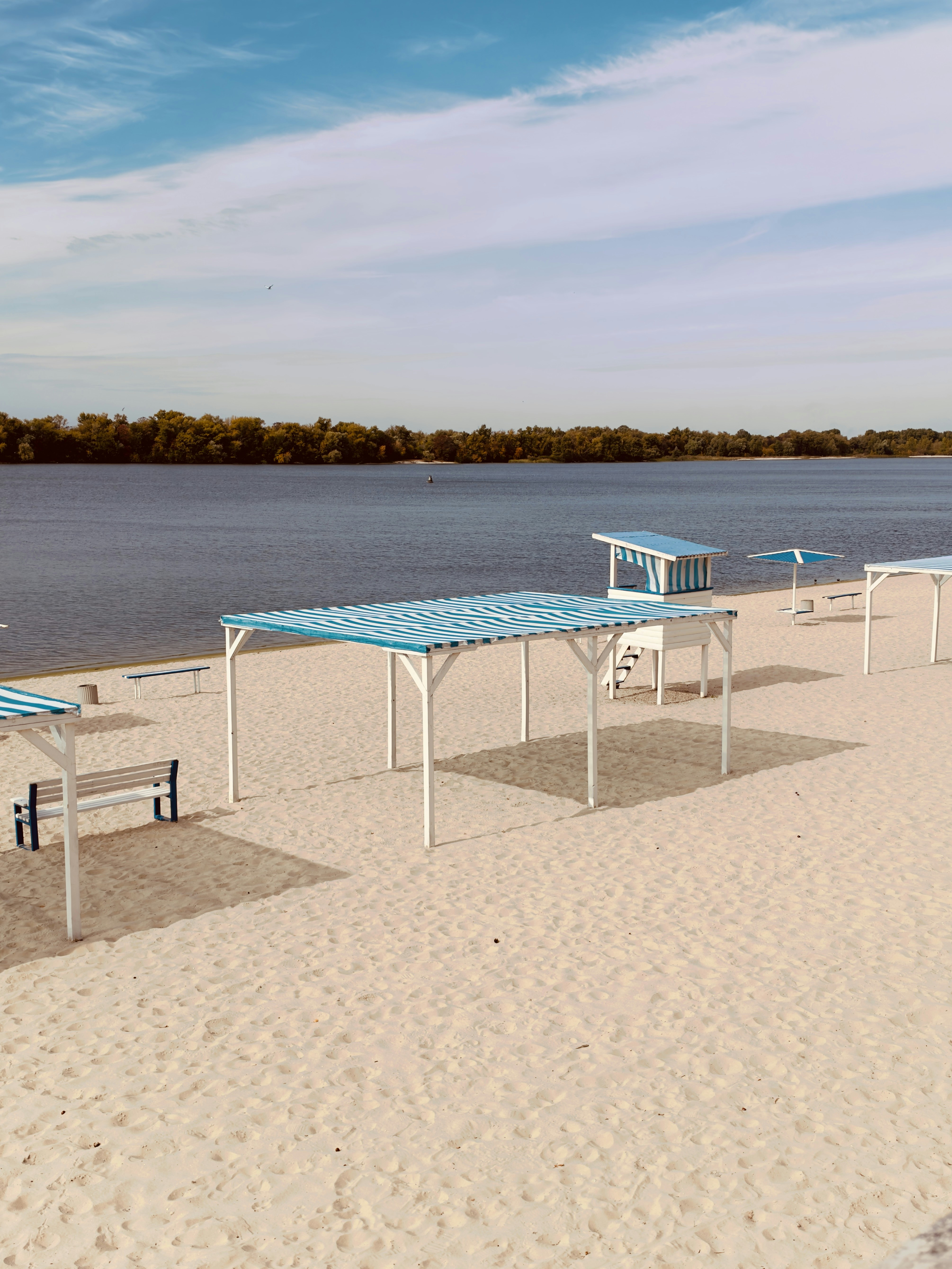 Blue and white striped canopies on a sandy beach beside a river