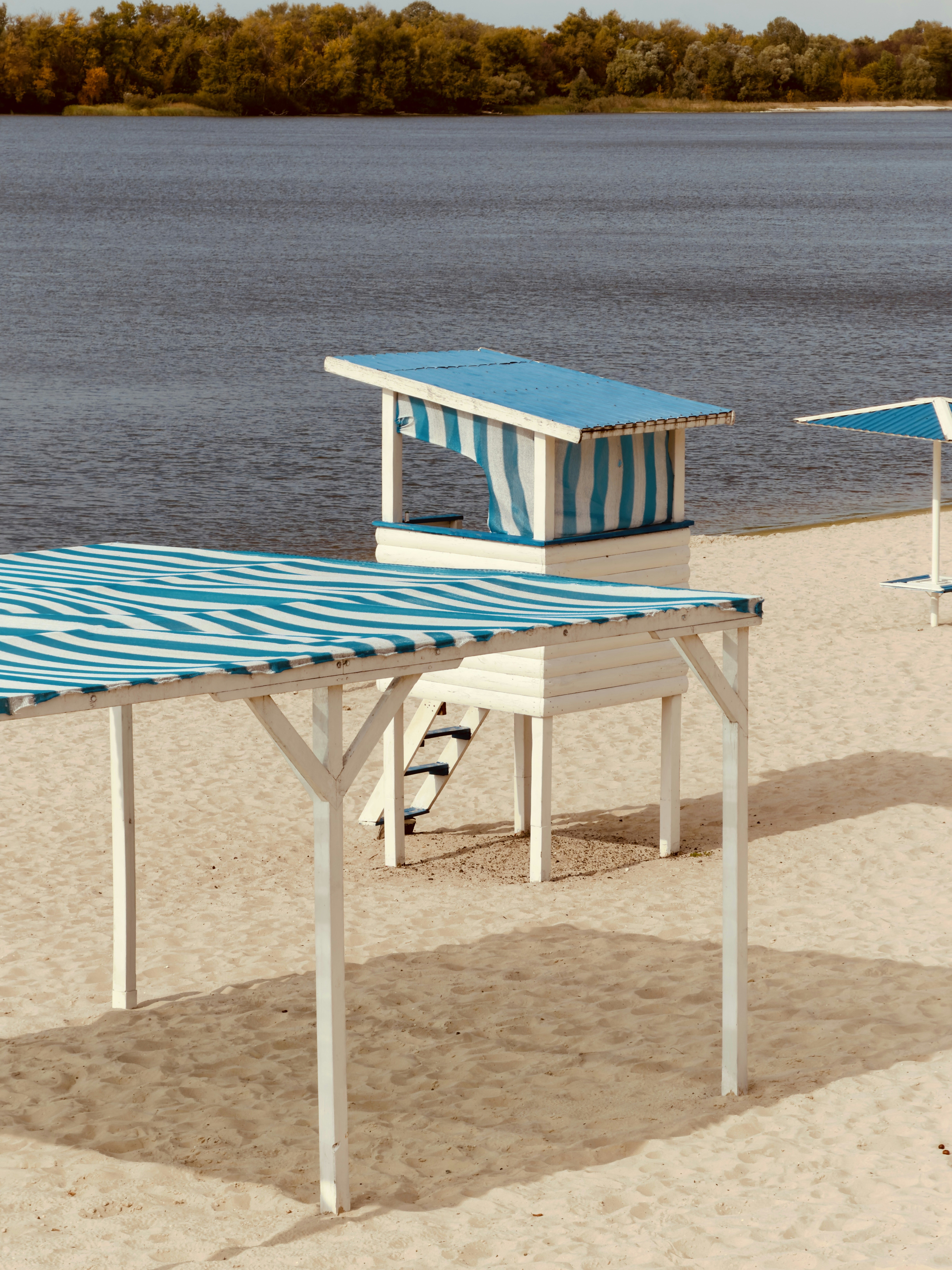 A blue and white striped lifeguard tower and beach canopy on sandy shore