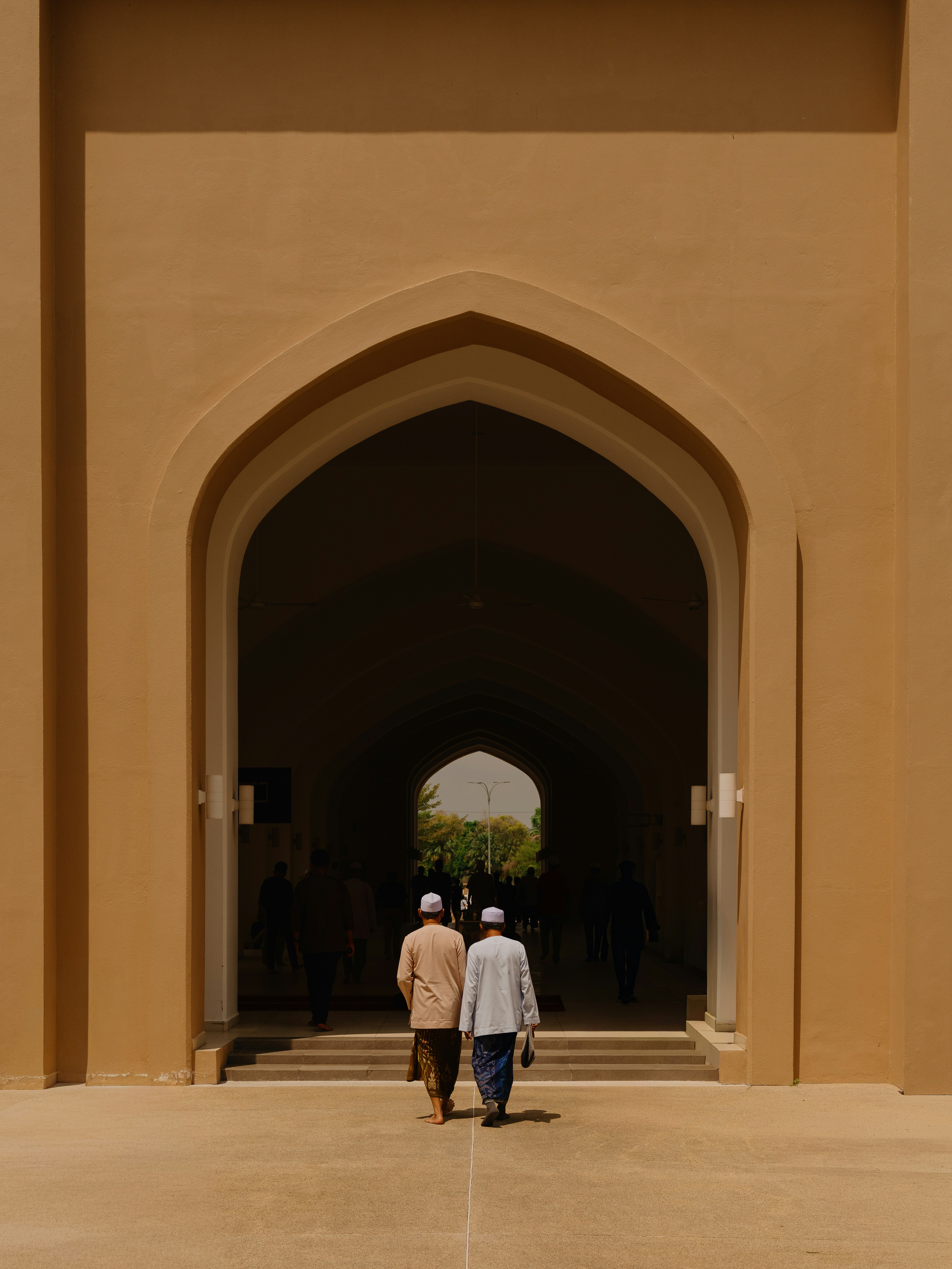 Two men in white kopiah walking through a large pointed archway at a mosque