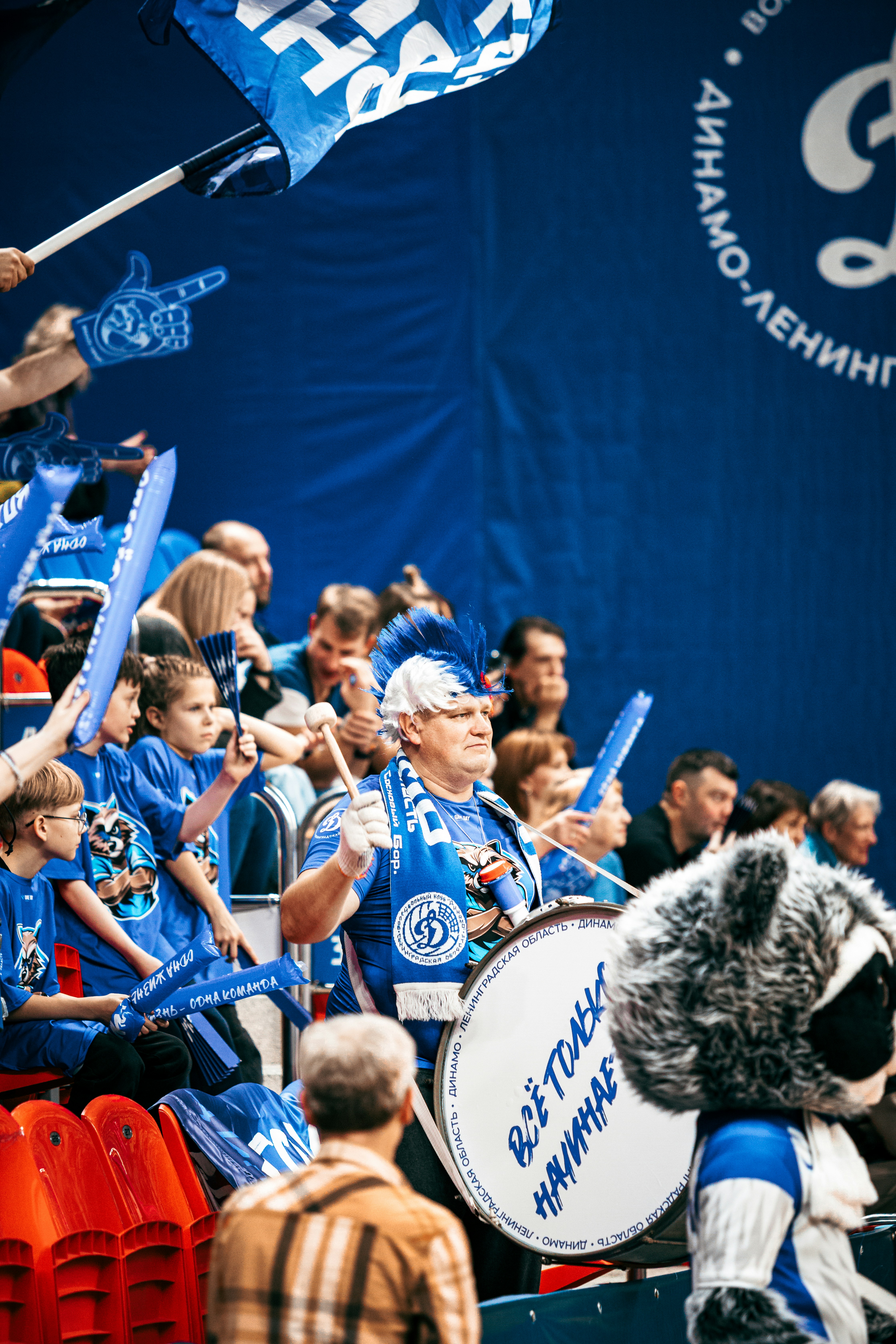 A man with a blue and white mohawk playing a drum in a crowd
