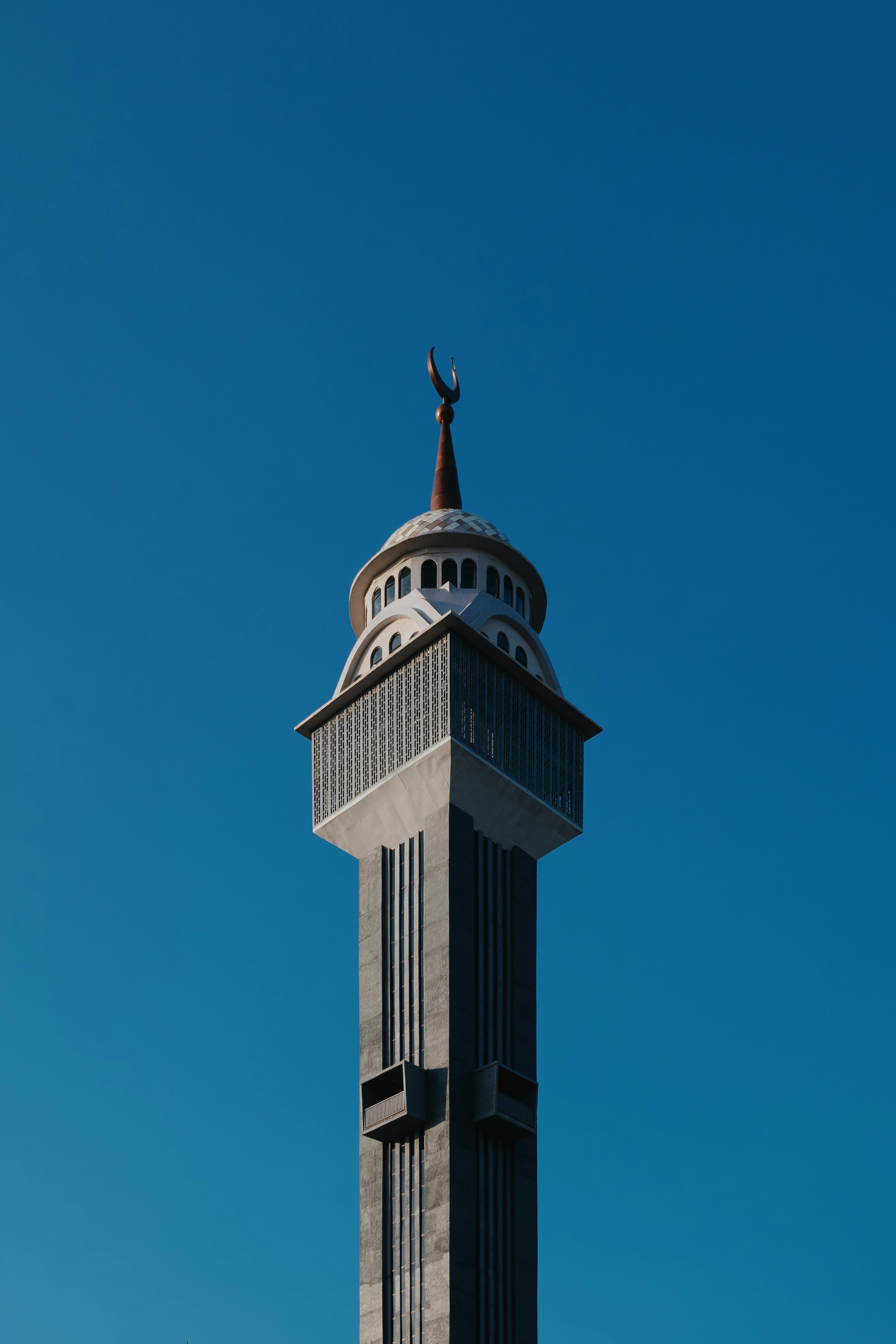 A slender minaret with a crescent moon finial against a clear blue sky