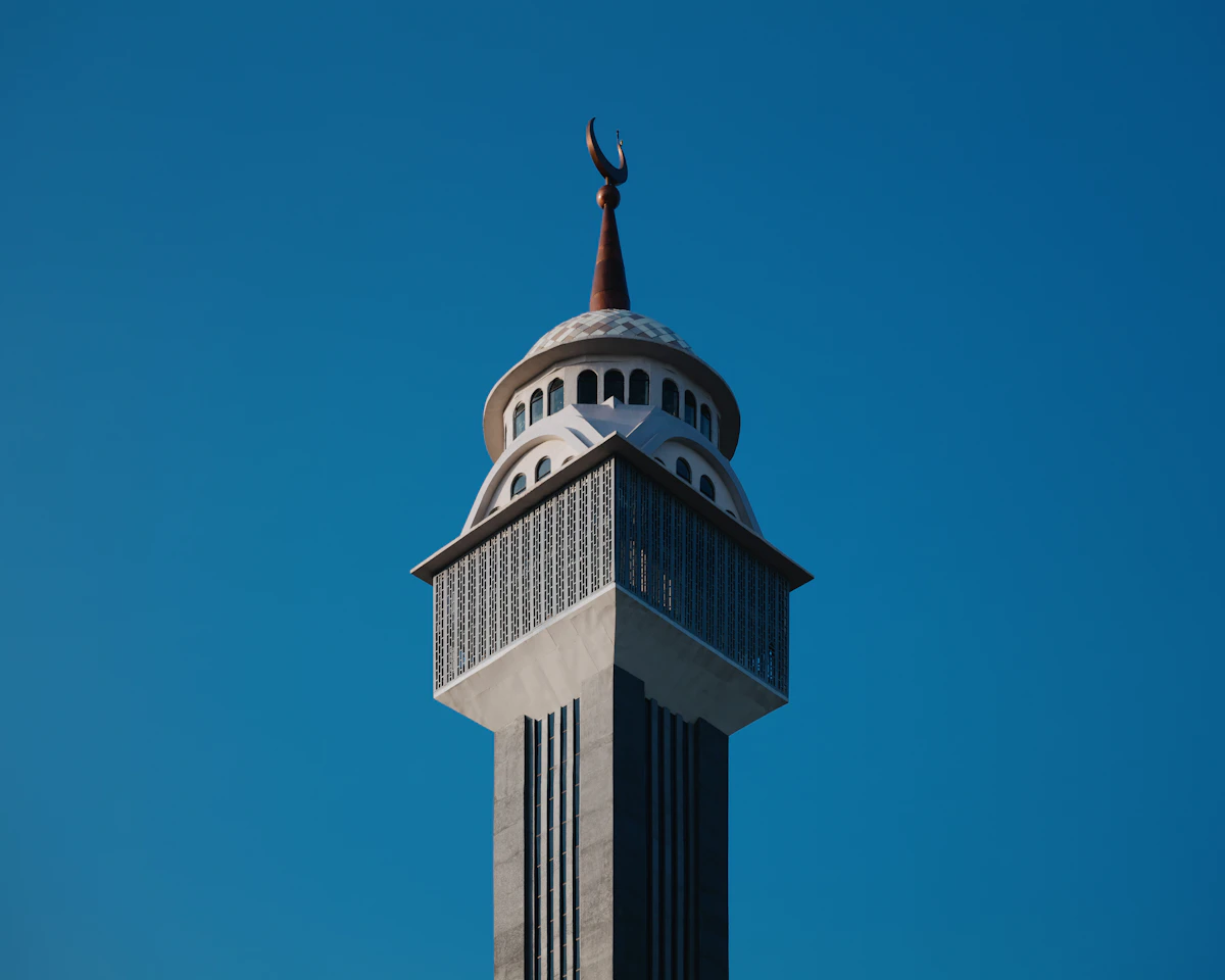 Puncak menara masjid berhias bulan sabit di langit biru