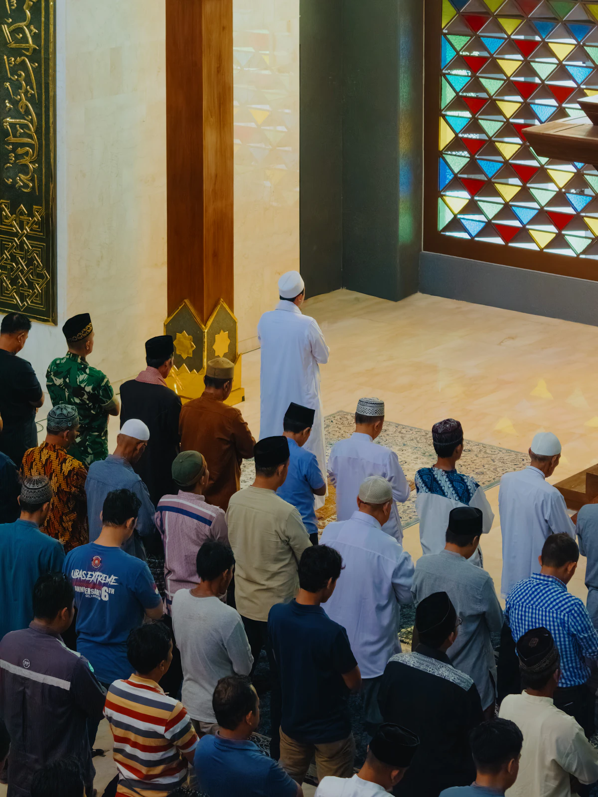 Barisan jamaah salat di bawah kaca patri masjid.