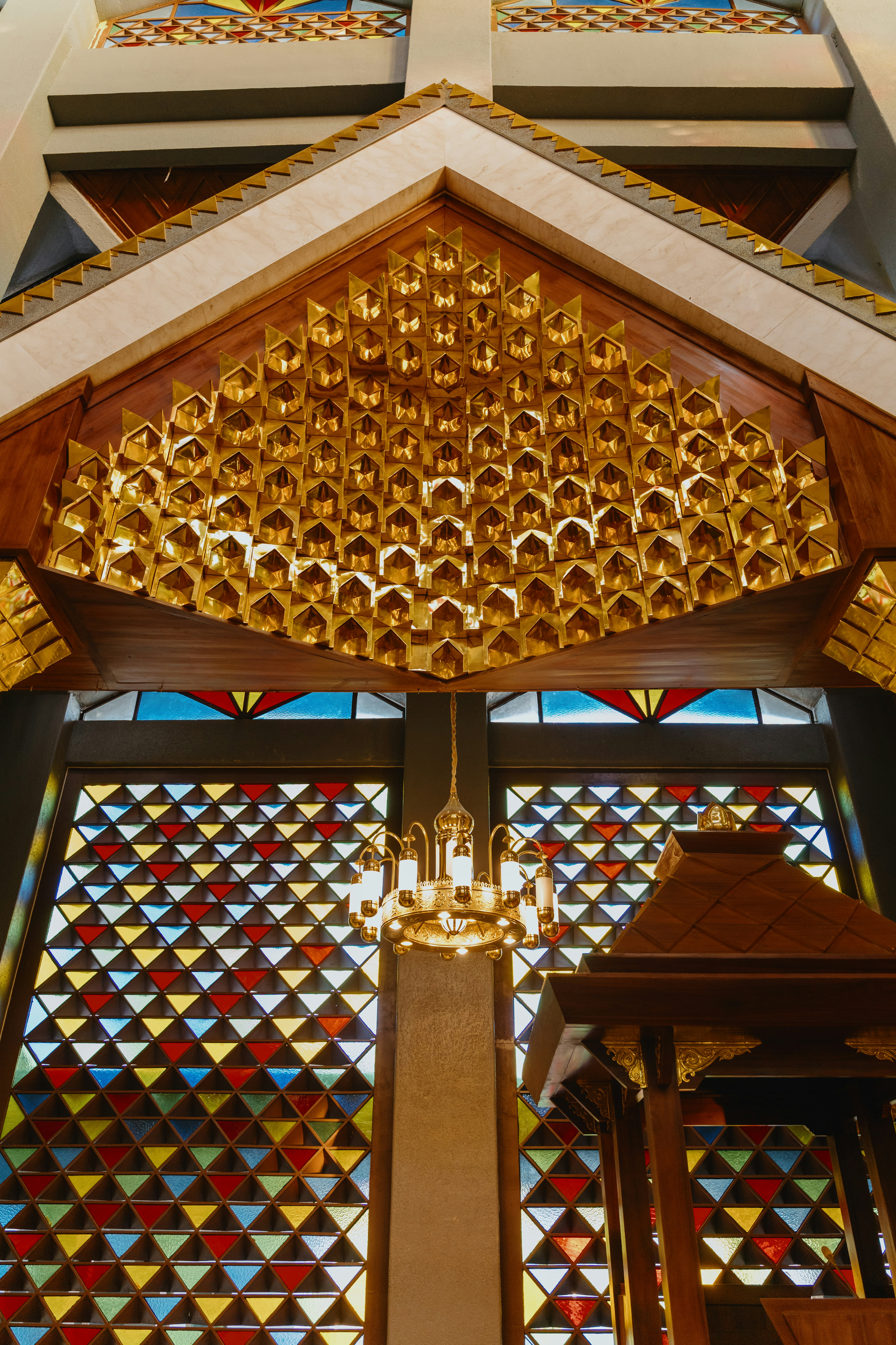 A golden carved mihrab above a chandelier and colourful stained glass windows